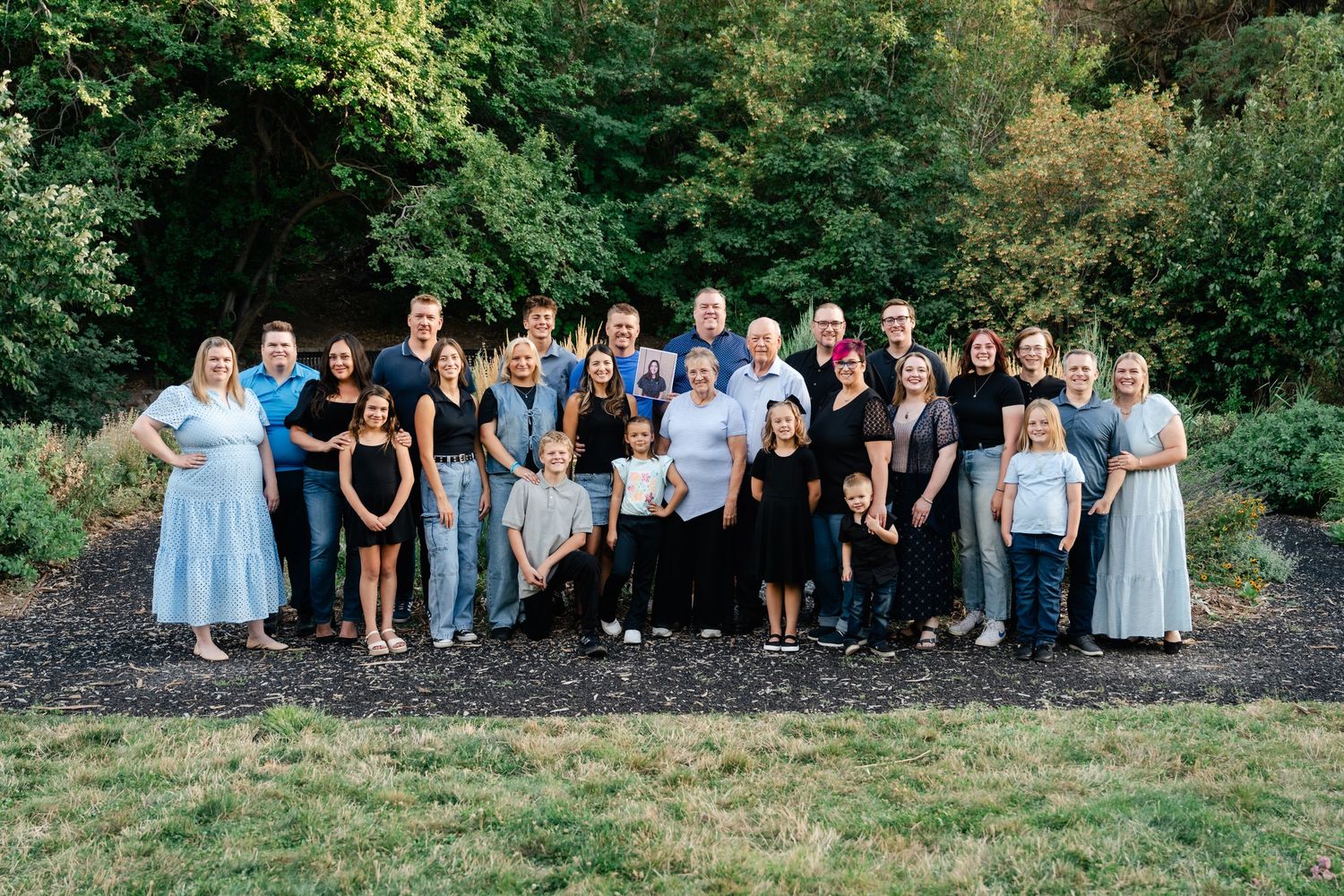 Large group of people sitting outdoors in a row on grassy hill during summer photoshoot.