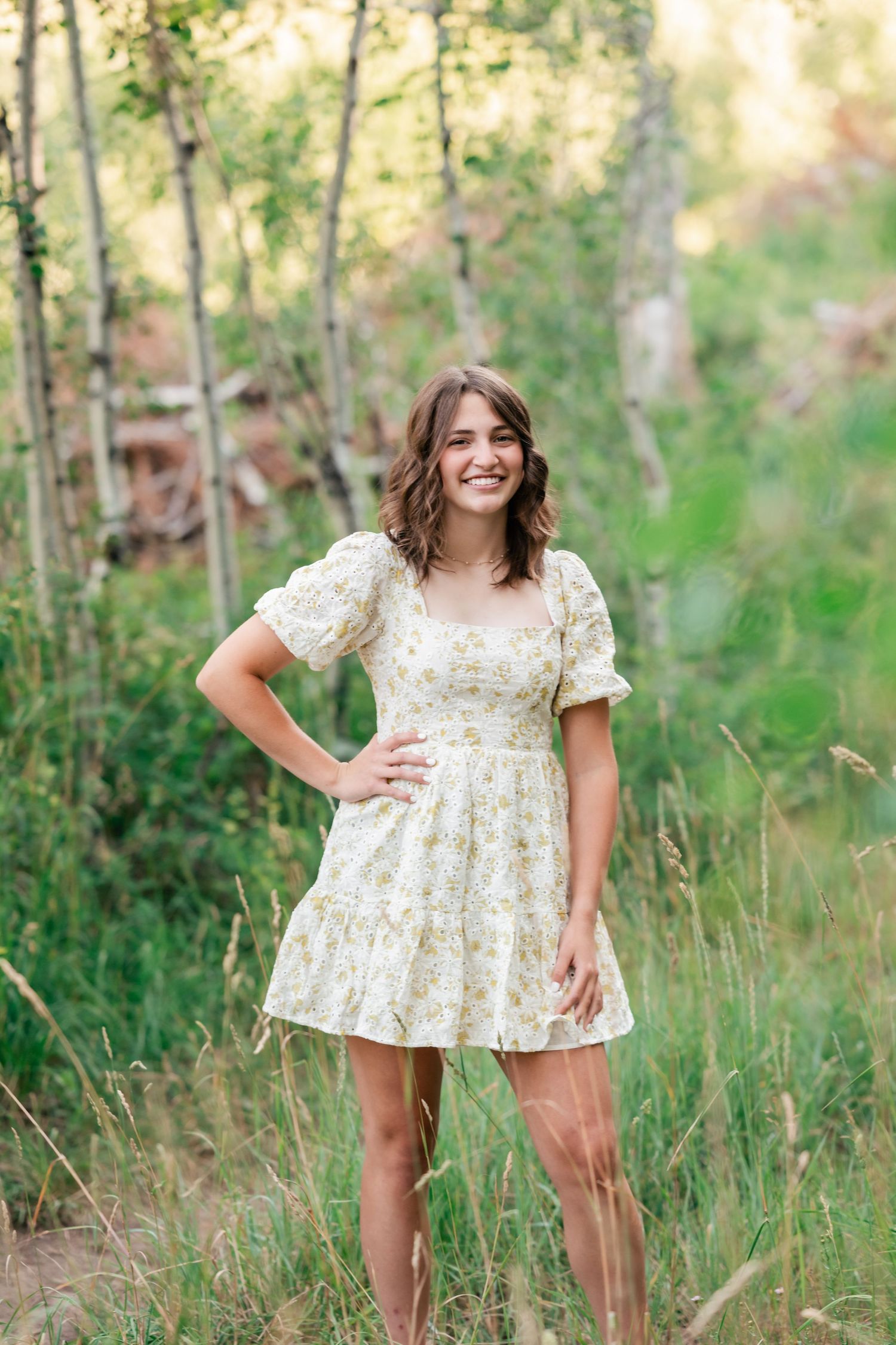 A floral babydoll dress is showcased in a series of outdoor poses among tall grass and trees in natural lighting.