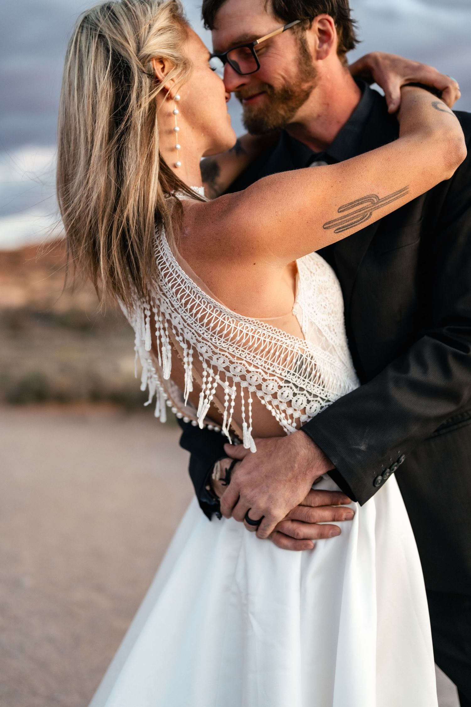 Intimate wedding couple embraces against a desert landscape backdrop at sunset.
