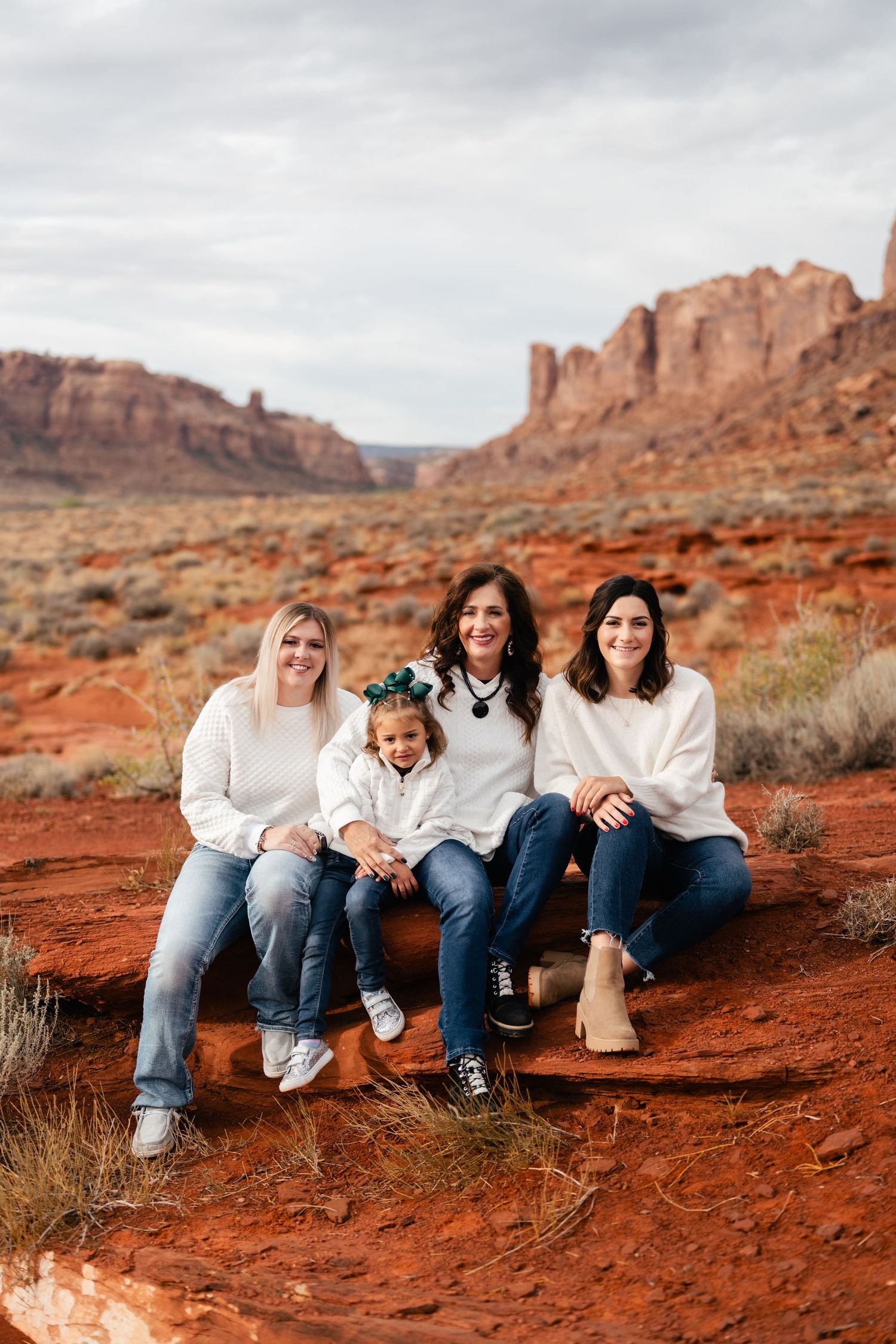 A group sits together on red desert rocks with towering sandstone formations in Monument Valley during sunset.
