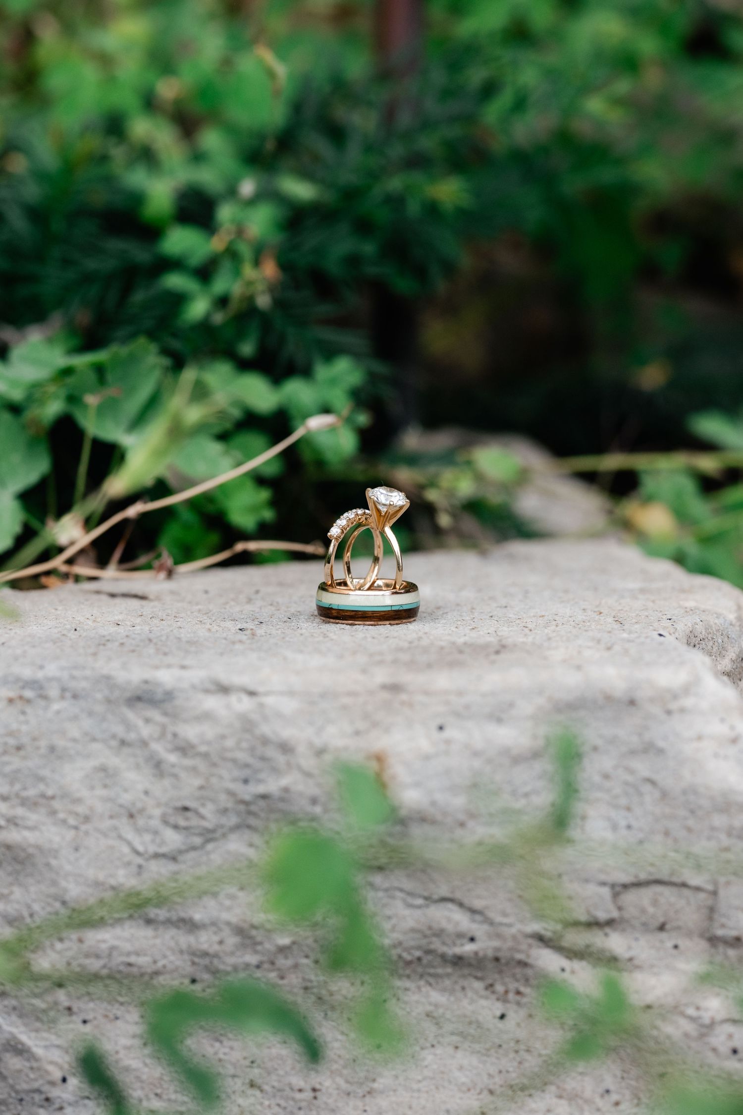 Wedding rings photographed on stone surface with soft green foliage bokeh in background.