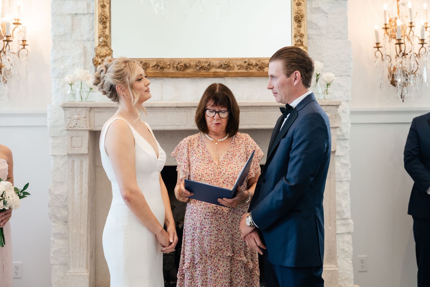 Wedding ceremony moments captured in an elegant white room with ornate gold-framed mirrors and crystal chandeliers.