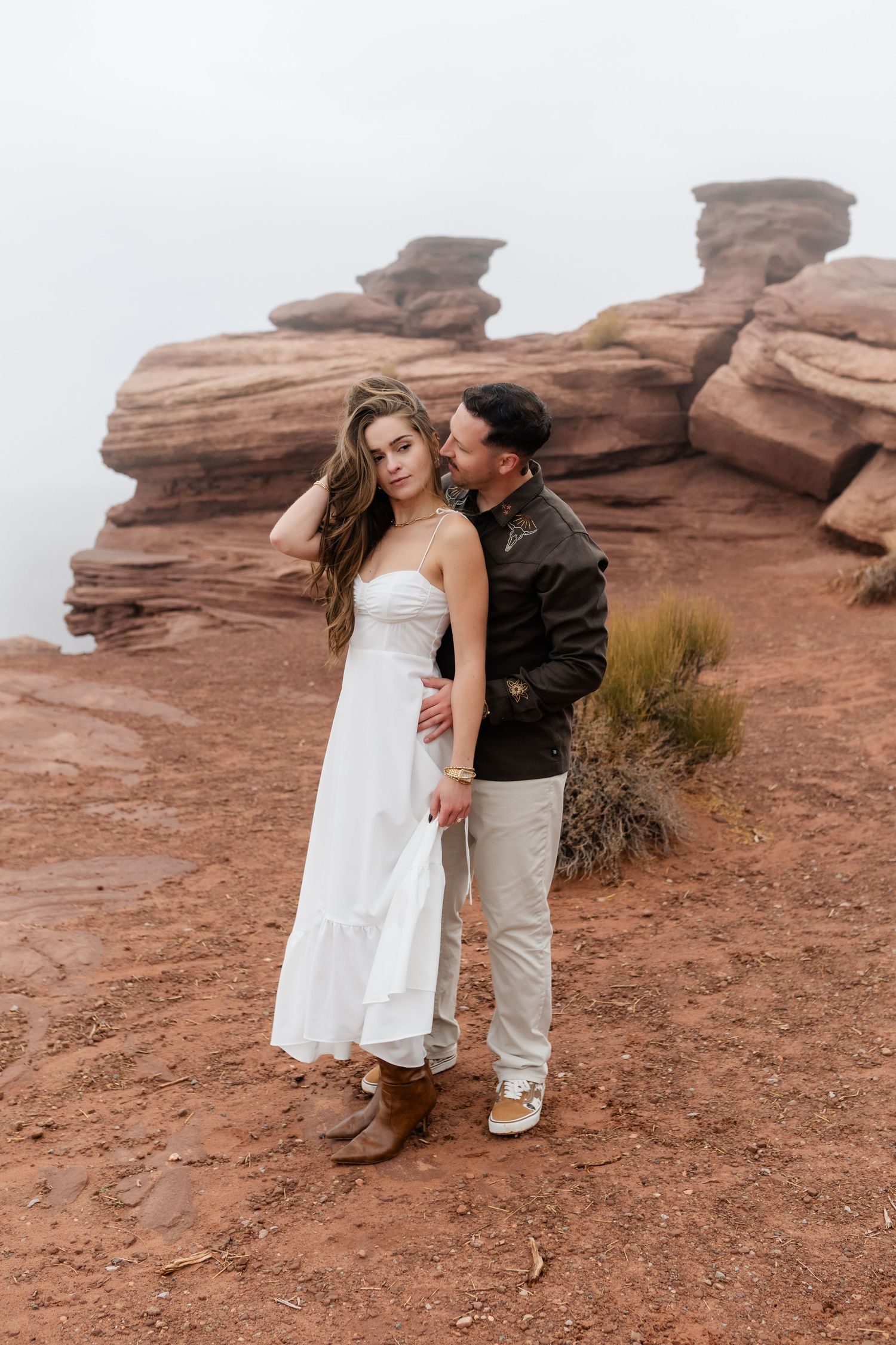 Couple in formal attire posing together against dramatic desert rock formations.