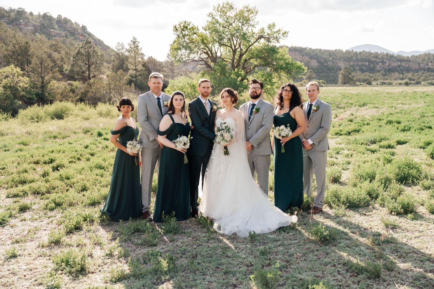 Wedding party gathers on a grassy hillside with scenic mountain views in the background.
