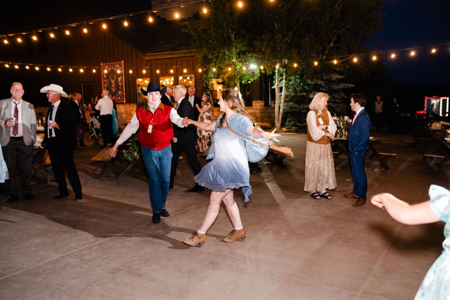 Evening wedding reception with string lights illuminating guests dancing on an outdoor patio.