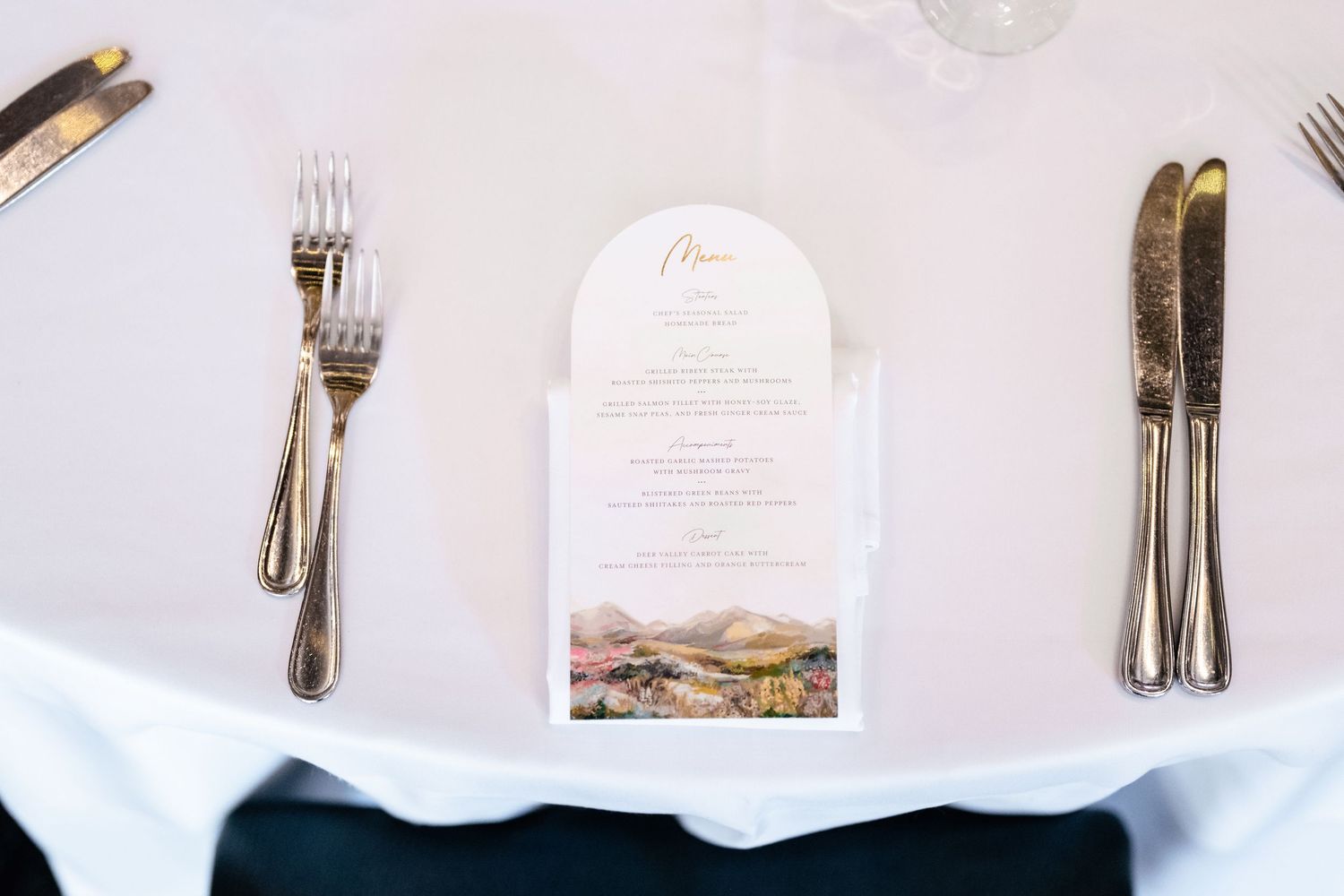 Elegant place setting with silver cutlery and white menu card arranged on crisp white tablecloth.
