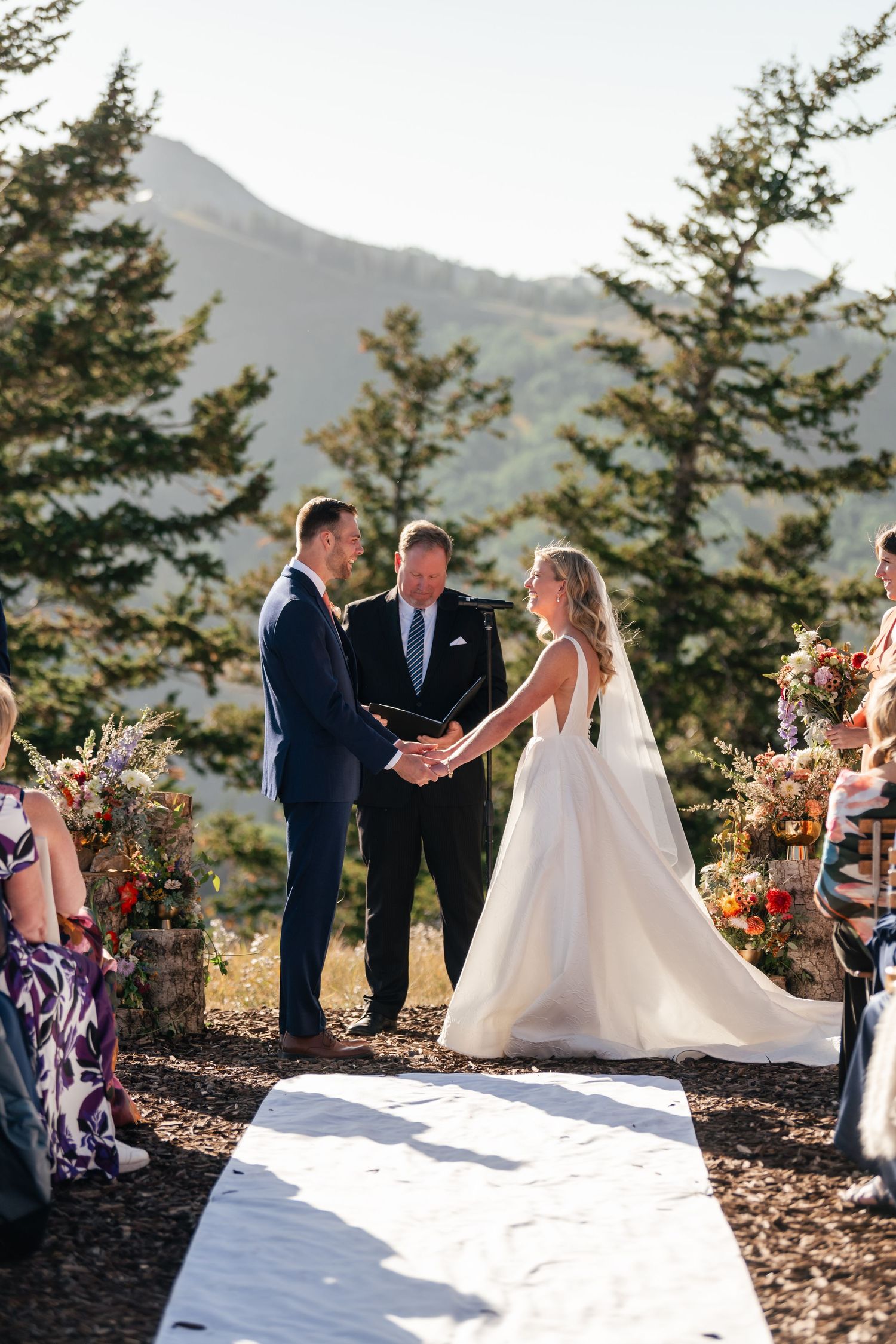 Mountain wedding ceremony with white aisle runner and evergreen backdrop.