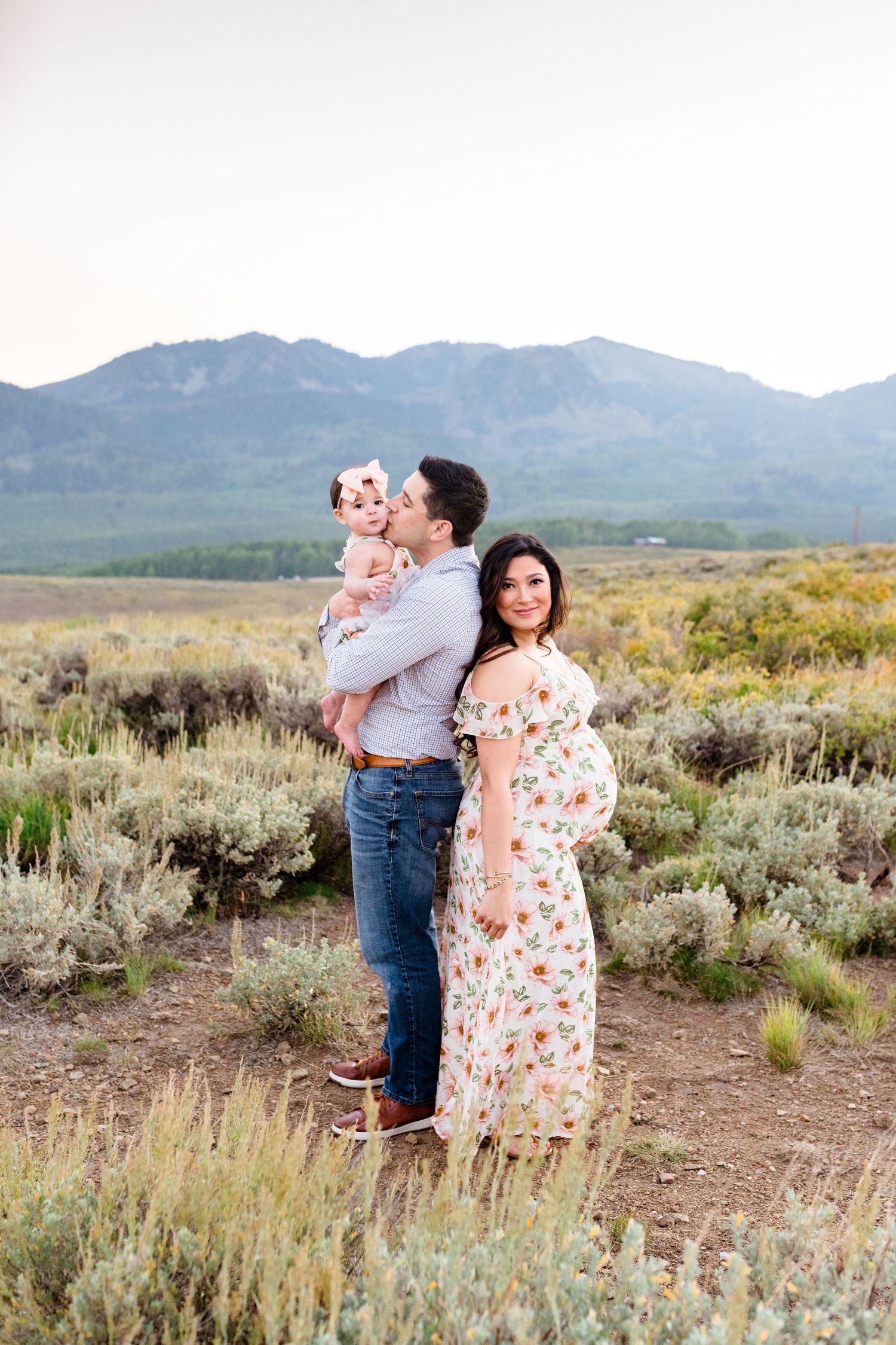 A family poses together in a desert landscape with mountains and sagebrush in the background at sunset.