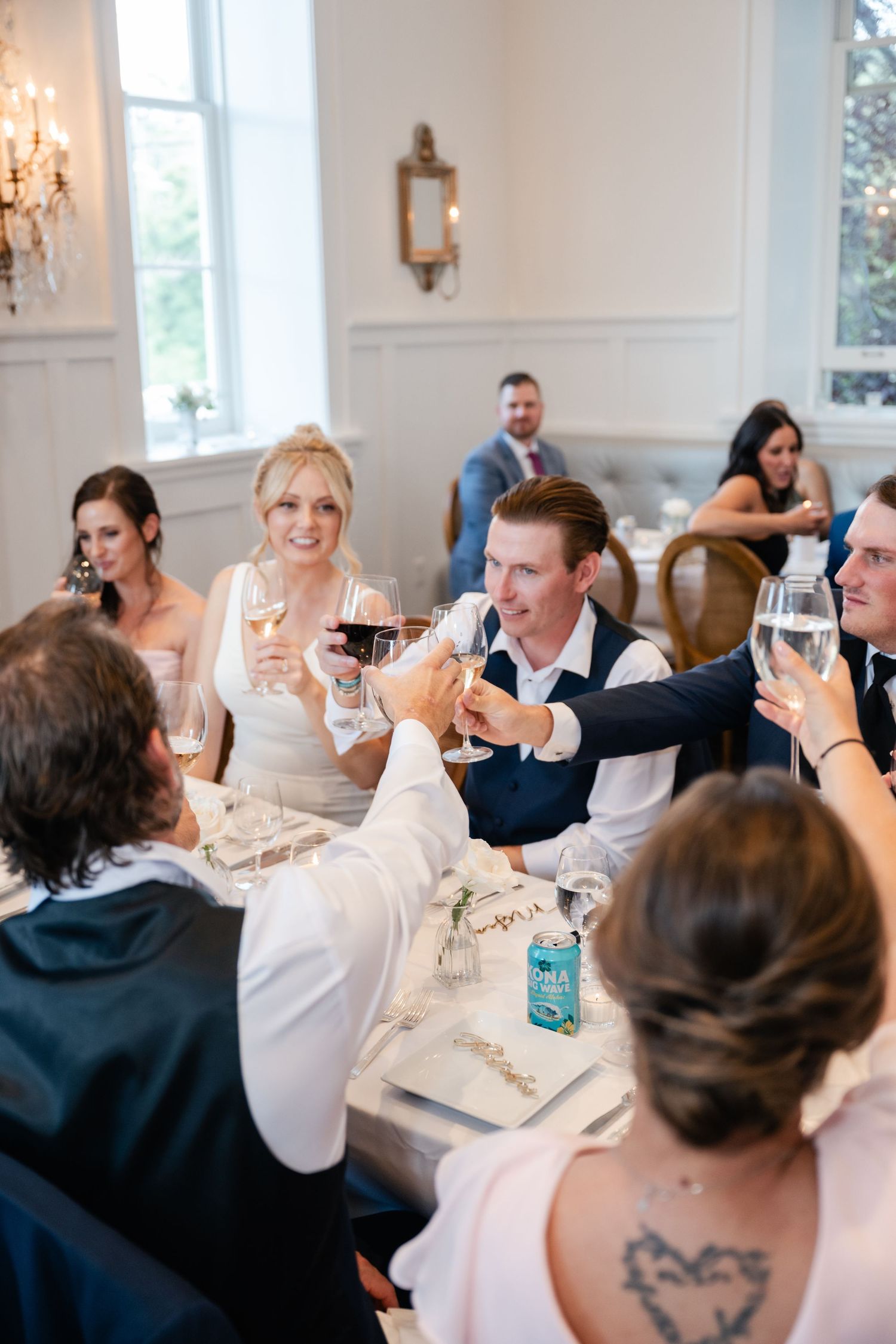 Wedding guests raising glasses in a toast at an elegant reception dinner, bride smiling in white dress.