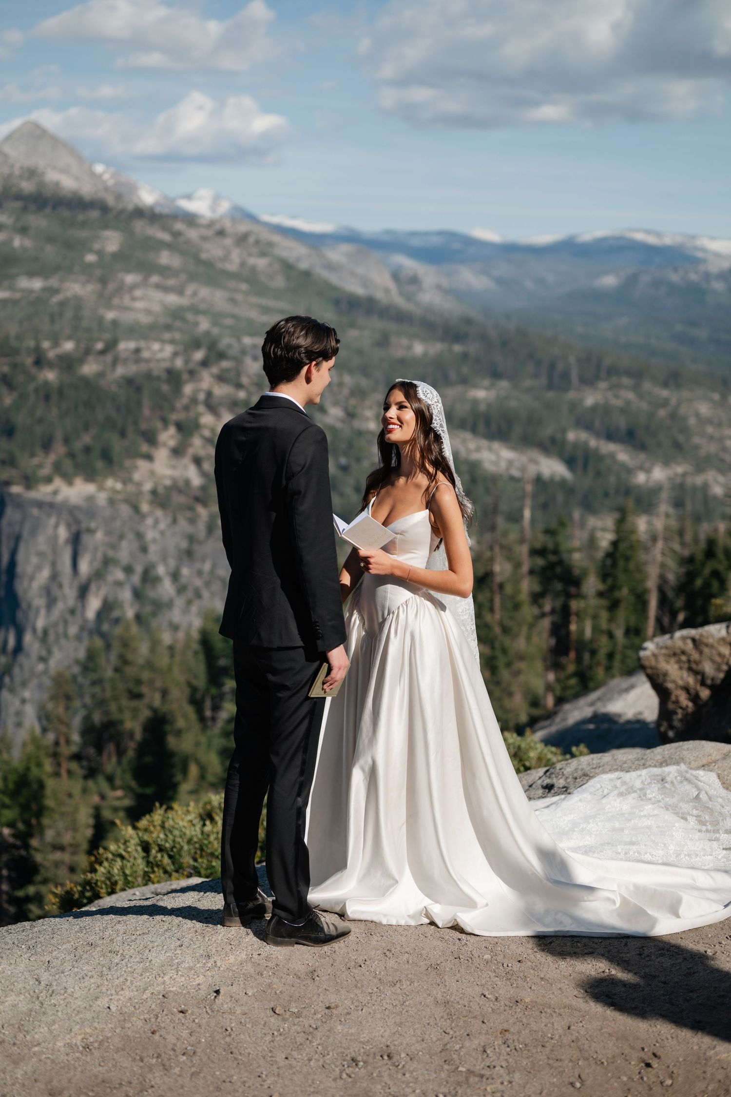 Bride and groom exchange vows on a rocky overlook with stunning mountain and forest views in Yosemite.