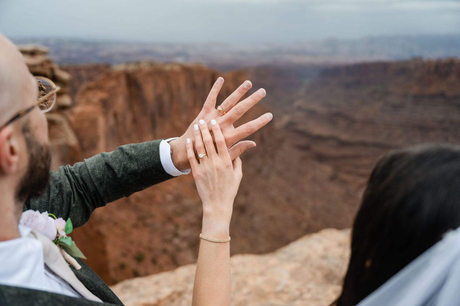 A group of raised hands reaching upward against a scenic desert canyon backdrop at sunset. Moab wedding photographer.