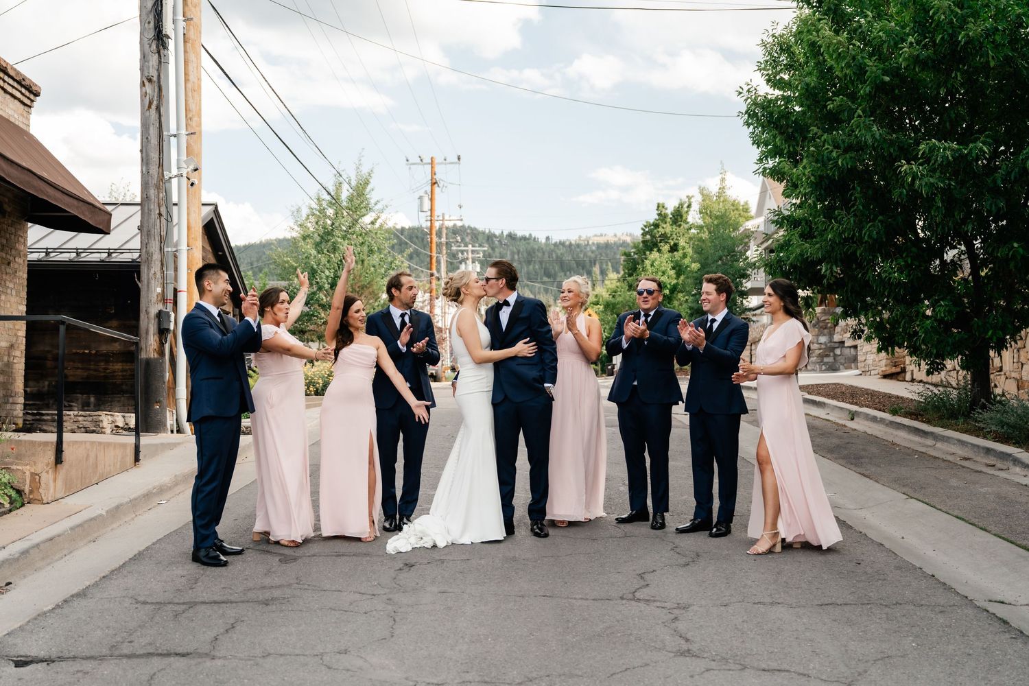 Wedding group arranged on steep city street with mountains and trees in background.