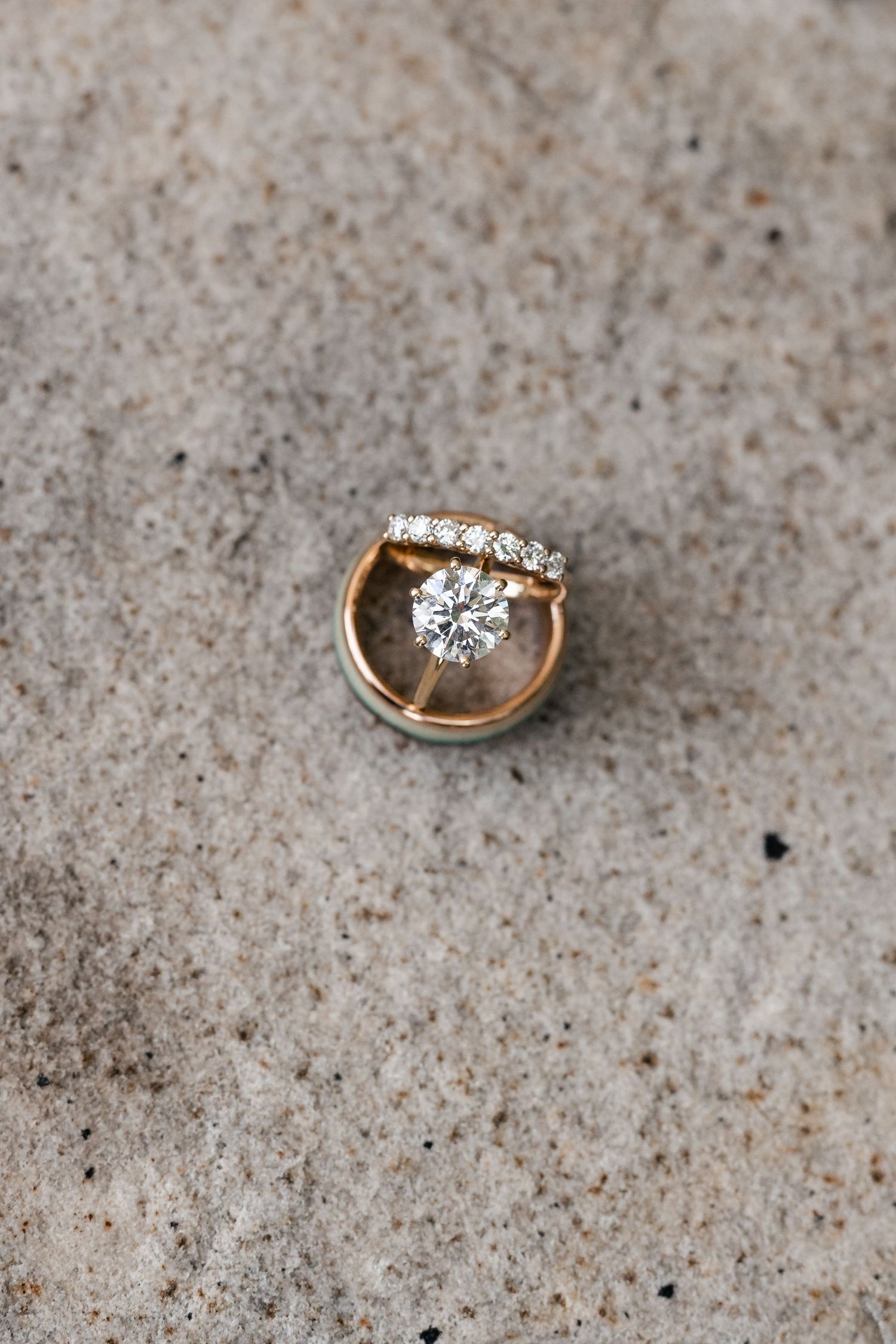 Gold wedding rings with diamonds photographed on a textured beige surface.