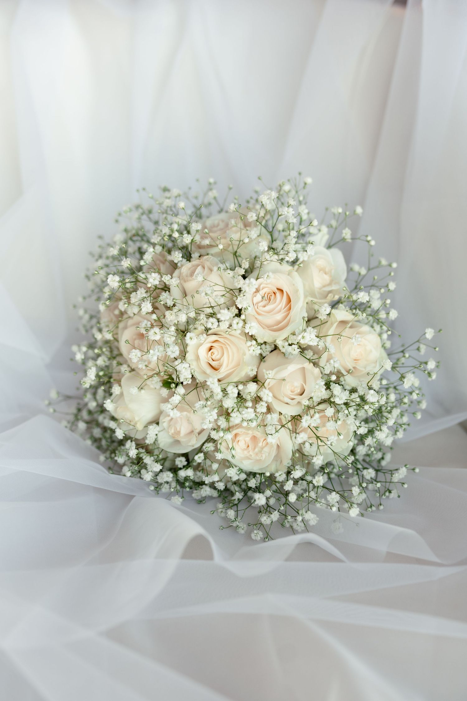 Romantic wedding bouquet featuring pale pink roses and delicate baby's breath against white fabric background.