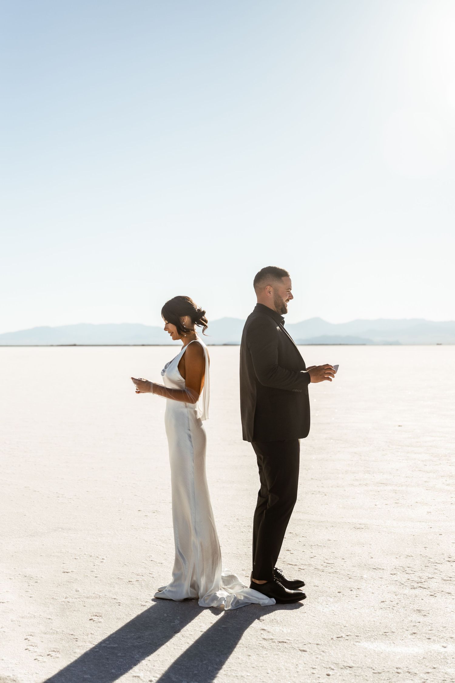 Wedding couple standing back-to-back on salt flats reading their vows.