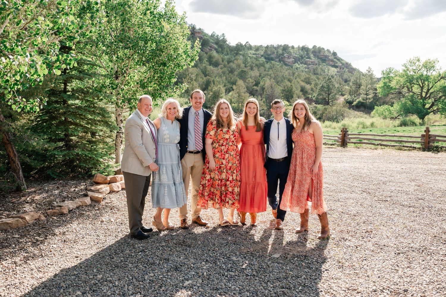 Group photo of wedding attendees in formal attire posing together on a gravel path.