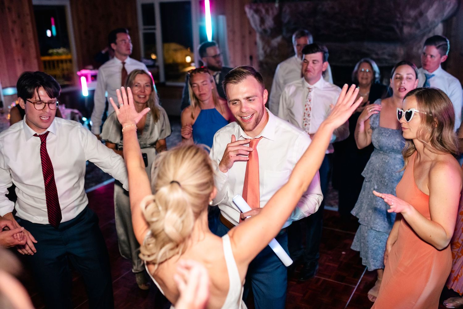 Lively dance party with guests celebrating under colorful lighting at a wedding reception.