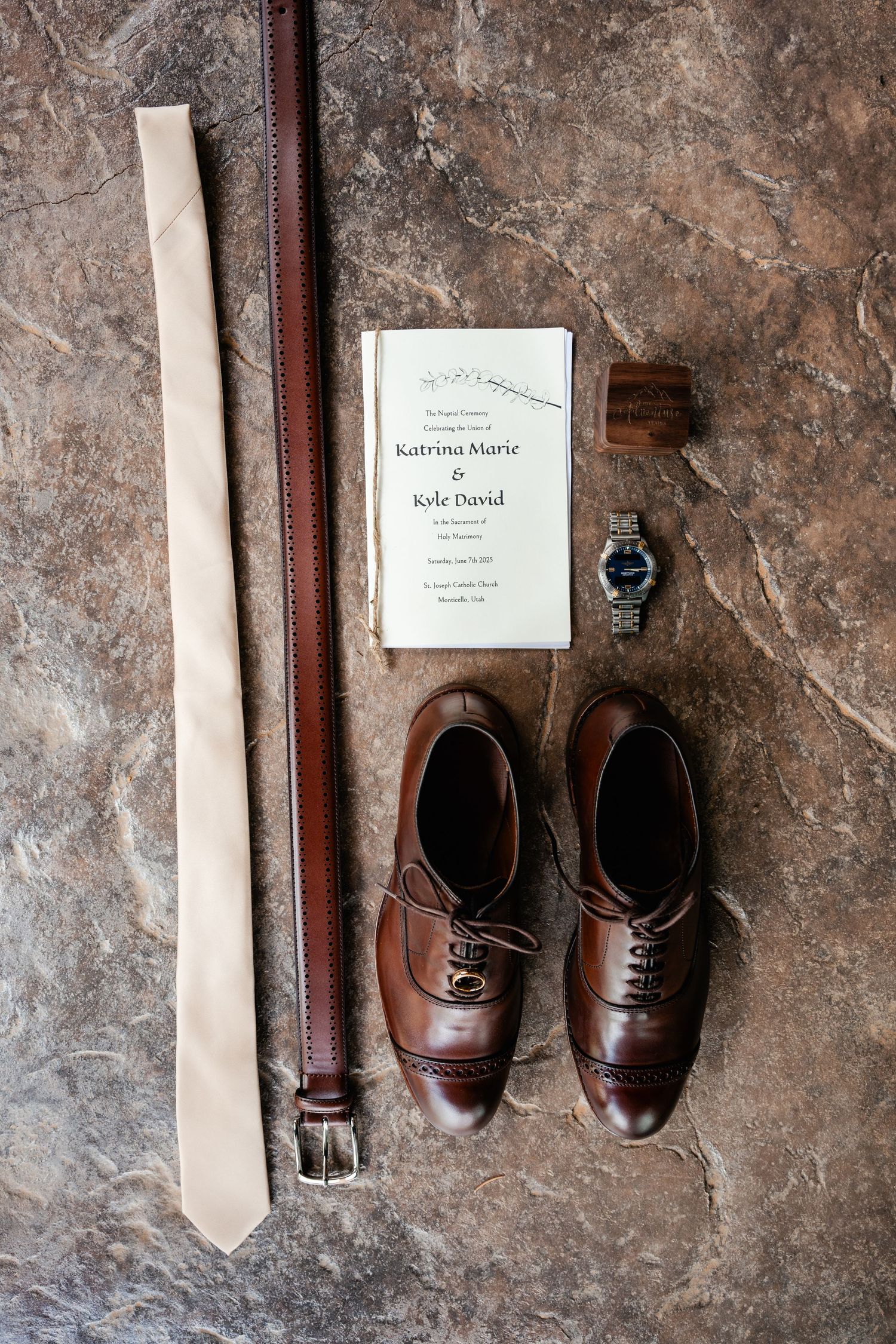 A series of brown leather dress shoes arranged against a textured stone wall with a sign.