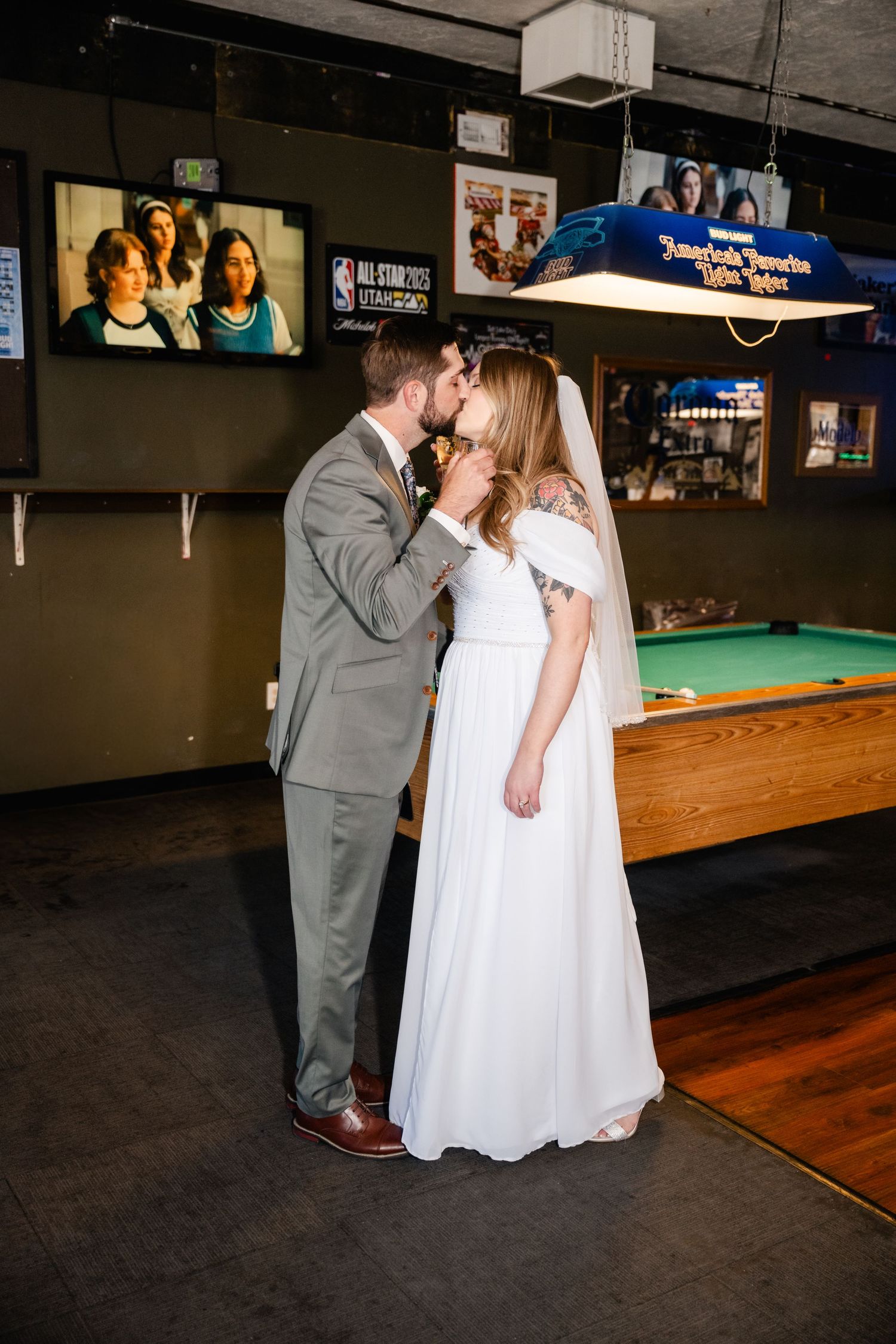 A romantic couple shares a tender moment while dancing in a casual bar setting with pool tables in the background.