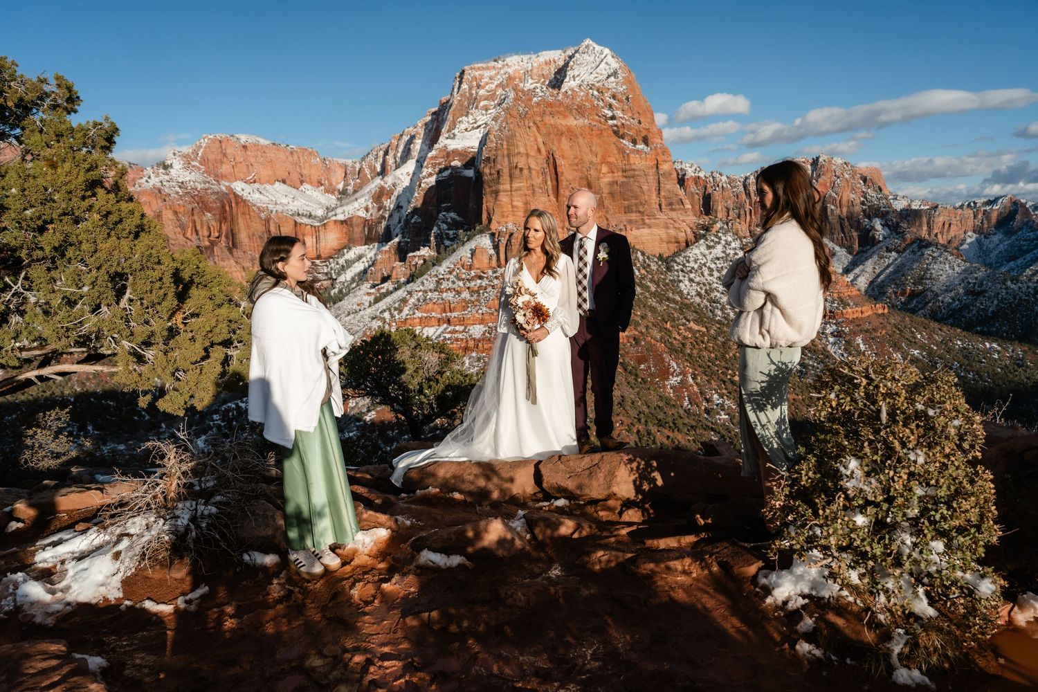 Wedding party poses on red rock overlook with panoramic mountain views in the background.