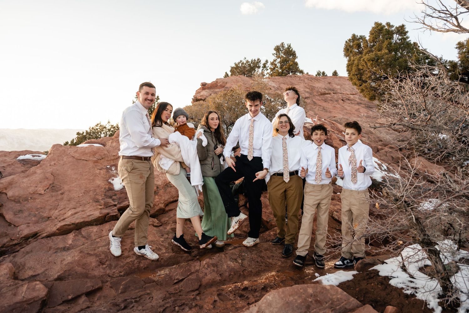 Wedding party poses on red rock formations with mountains in background.