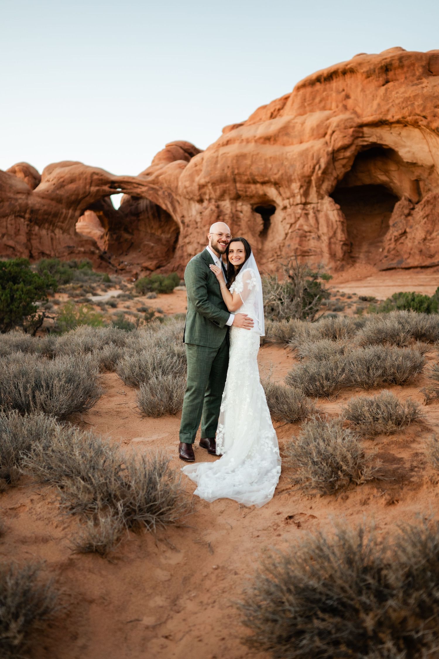 Wedding couple embracing against stunning red rock formations in a desert landscape.