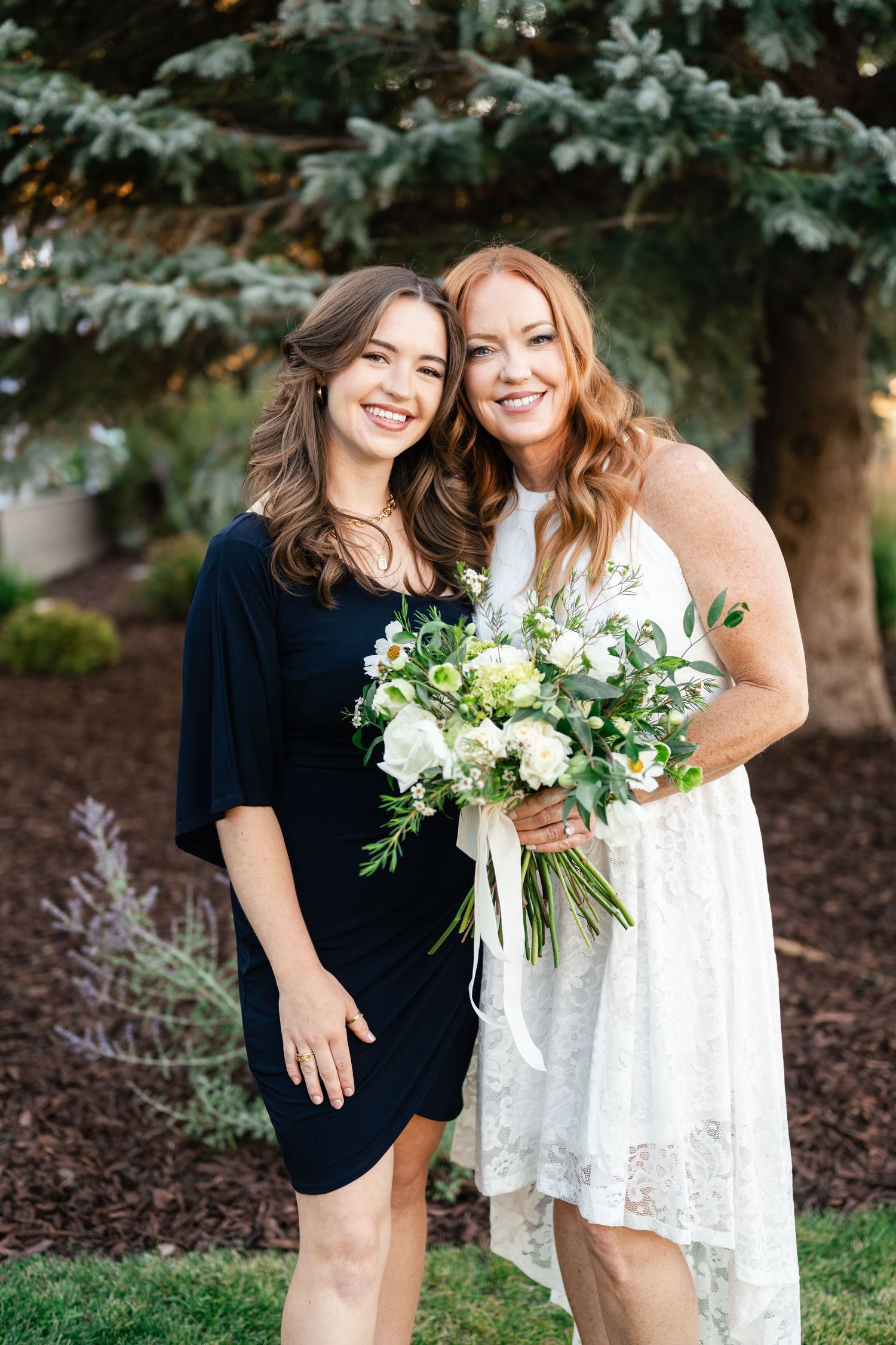 Two people posing with white floral bouquets against an outdoor garden backdrop.
