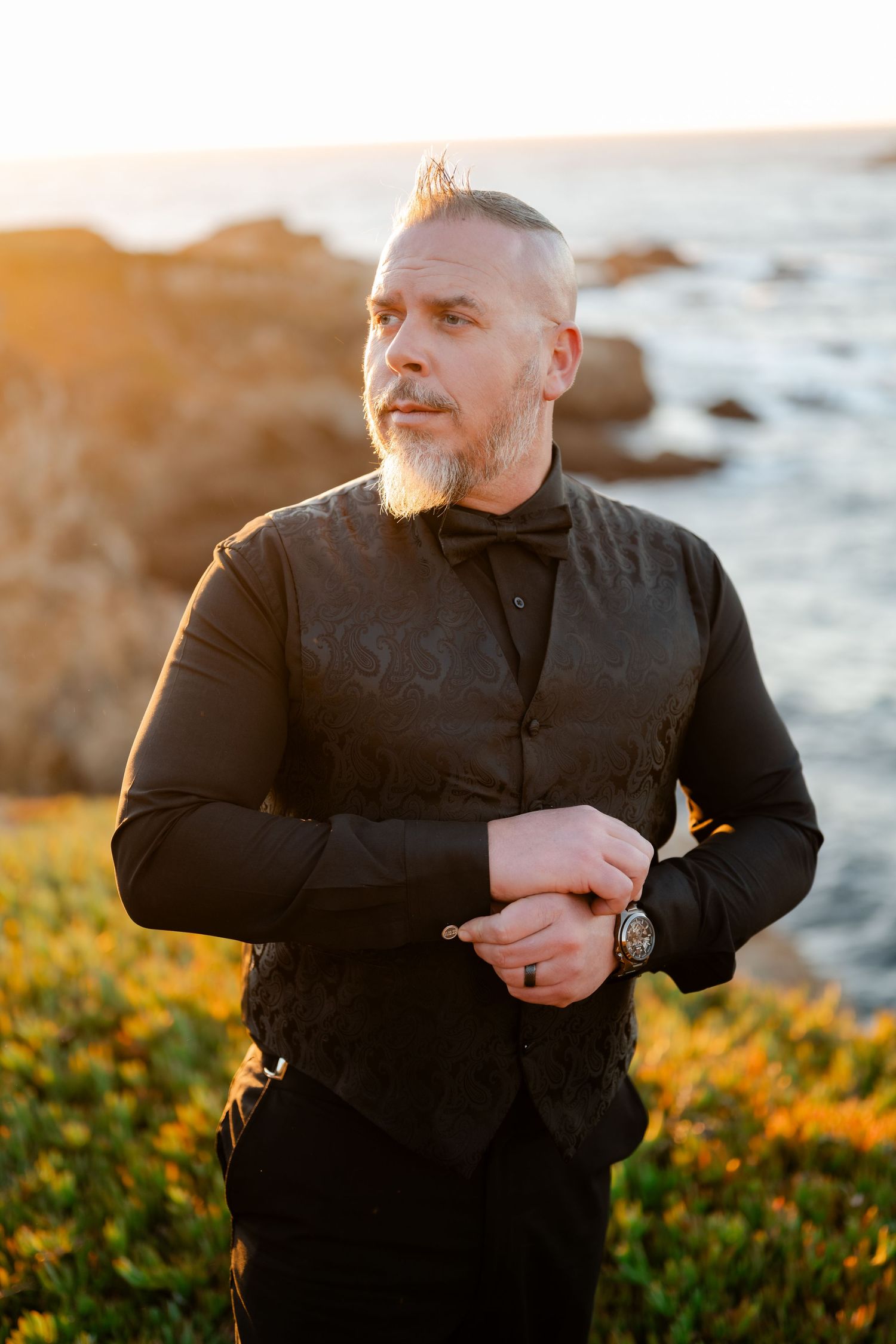 A stylish black dress shirt and watch against a scenic coastal sunset backdrop.