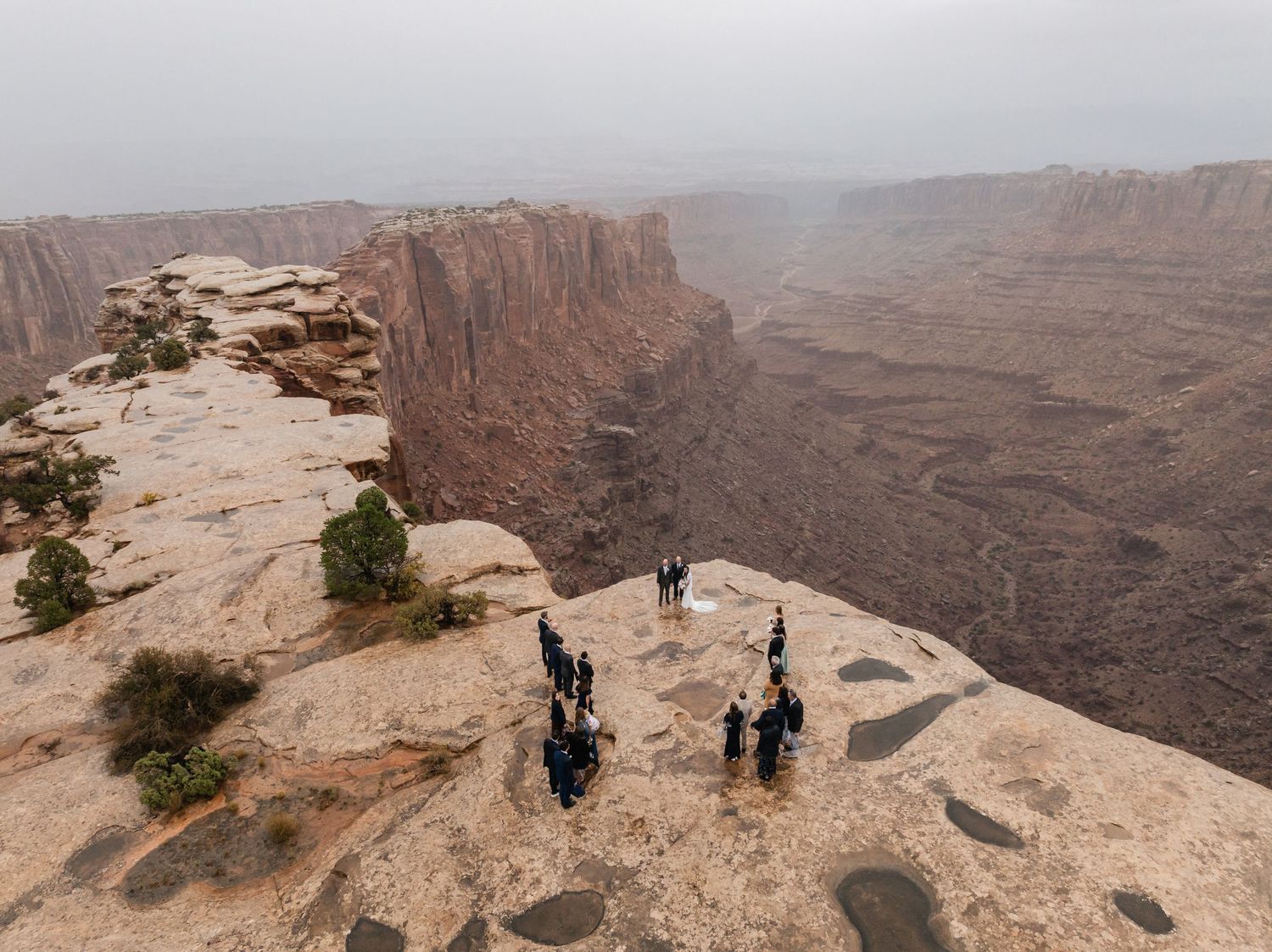 Small wedding group gathered on rocky overlook with vast canyon views in background.