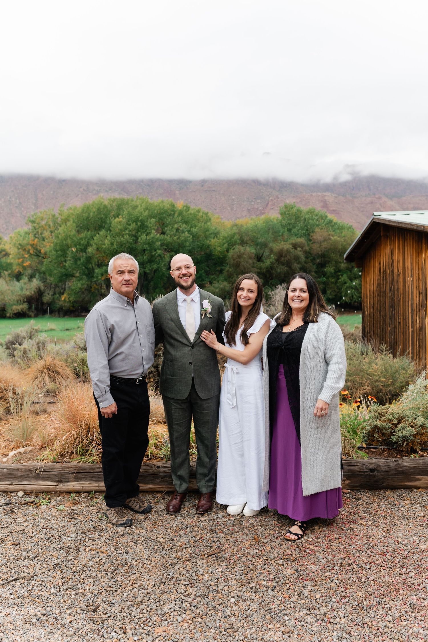 Wedding group photo with guests on a gravel path near a rustic wooden building.