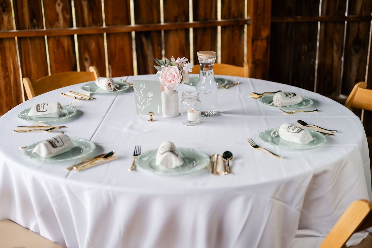 White round dining tables set for a wedding reception in a rustic wooden barn venue.