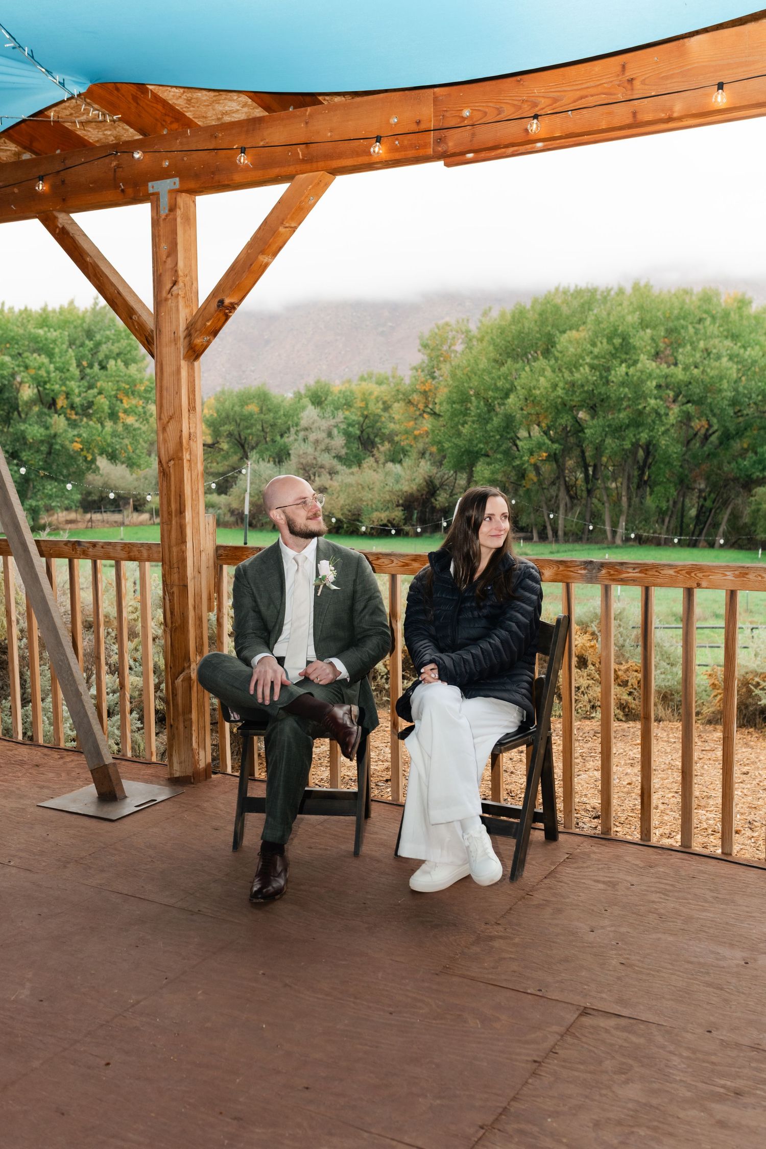 A couple shares a sweet moment on a rustic wooden deck overlooking a scenic landscape during their wedding celebration.