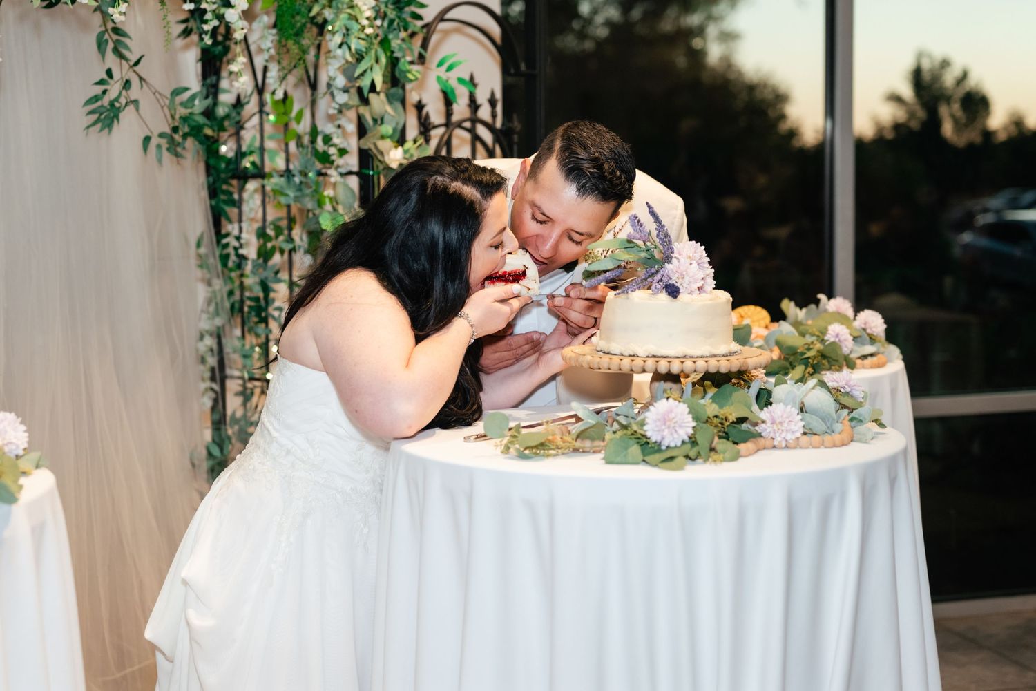 A bride and groom share their first bite of wedding cake together at an elegantly decorated reception table.