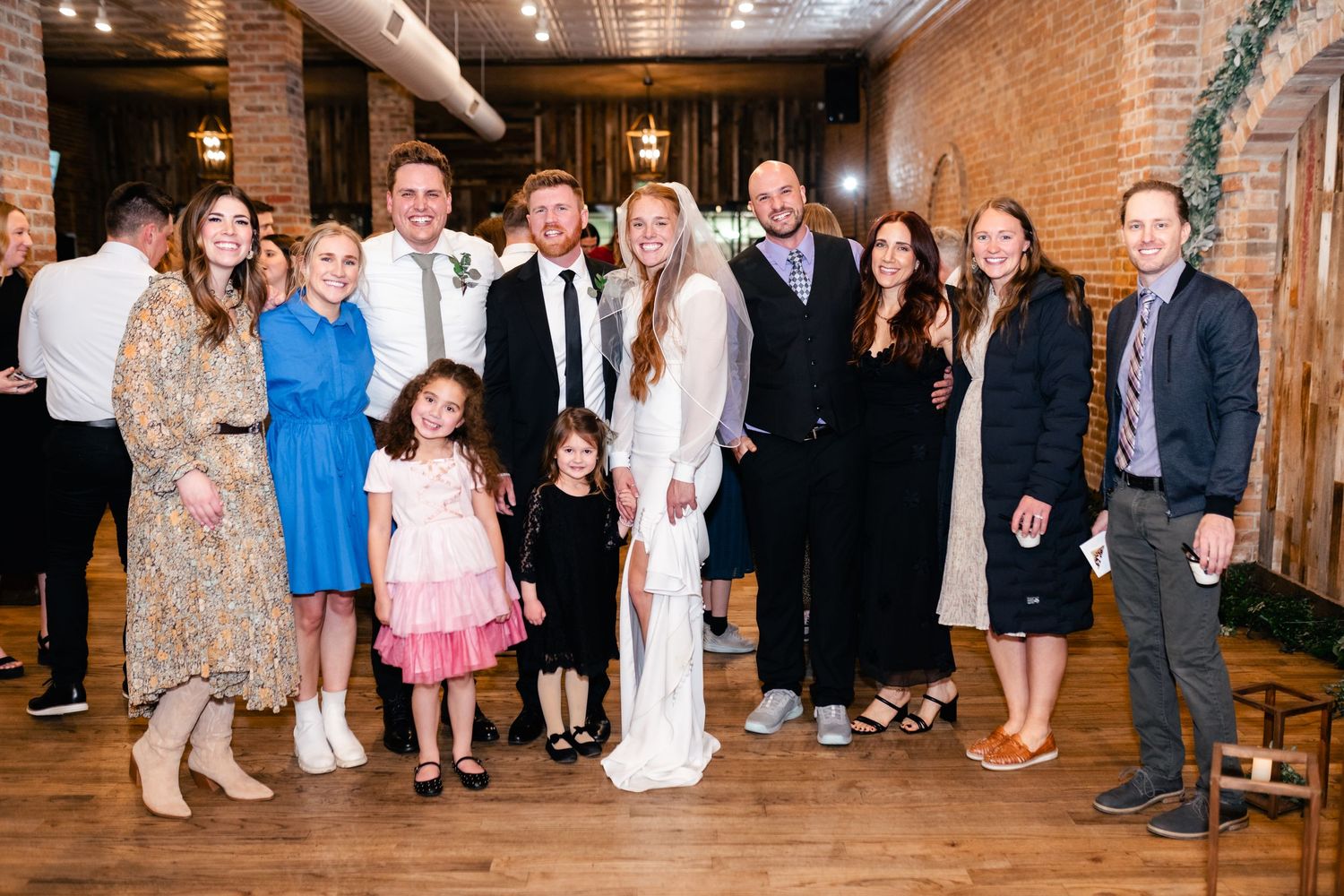 Wedding party poses together in rustic brick venue with exposed walls and wooden floors.