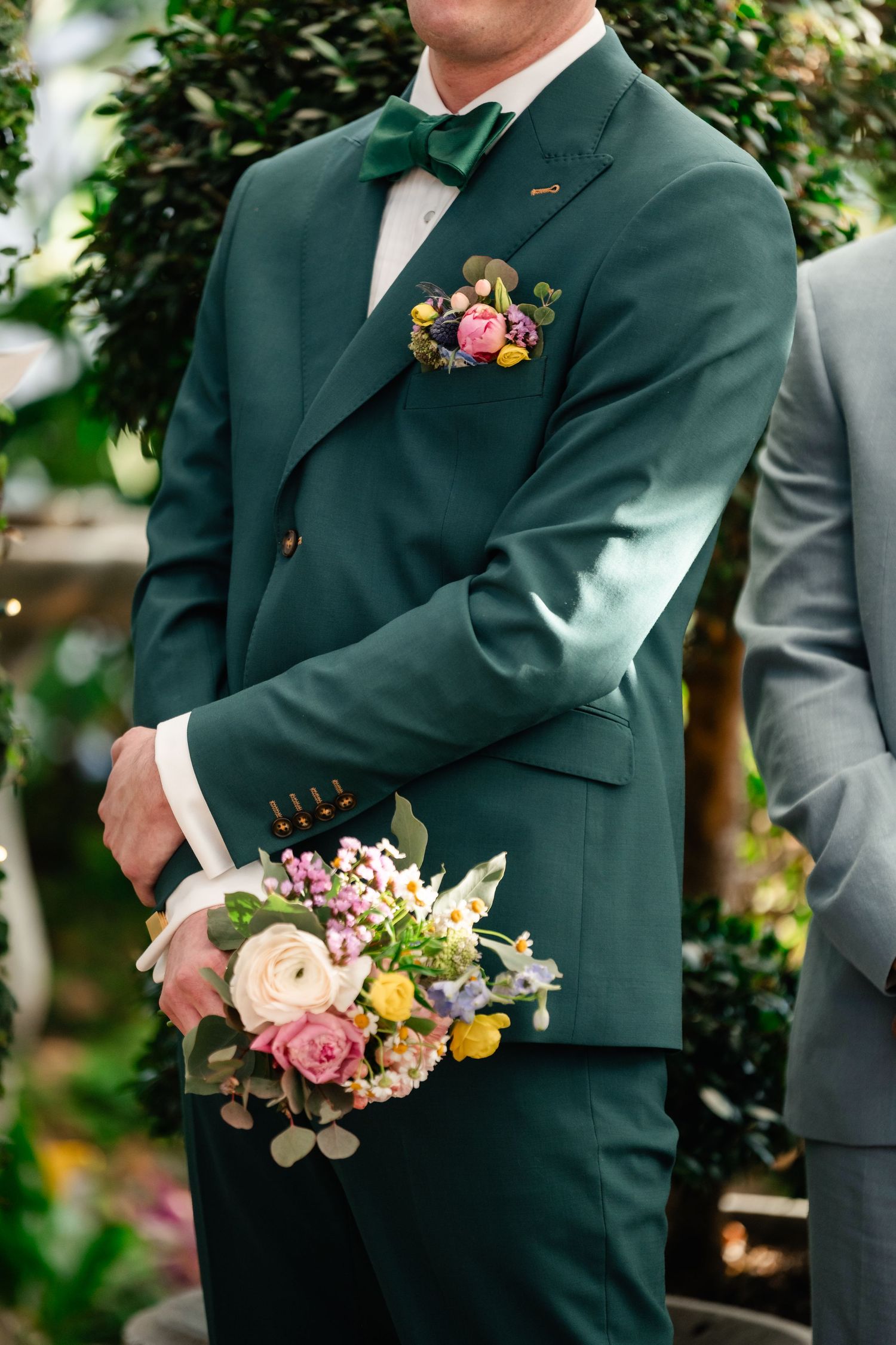 Close-up of emerald green wedding suit with colorful floral boutonniere and pocket square.