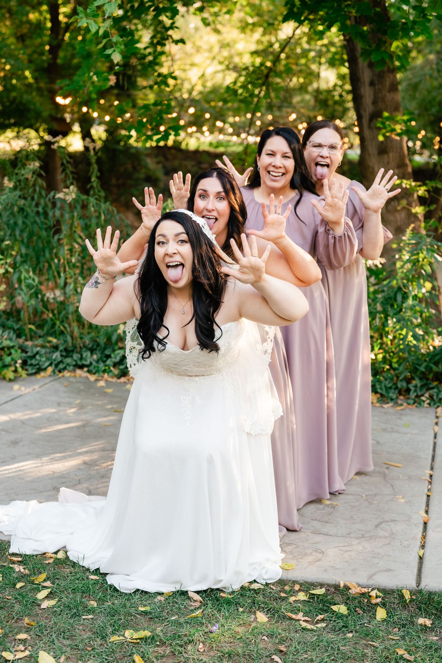 A bride and bridal party in pink dresses wave excitedly at the camera during an outdoor wedding photo session.