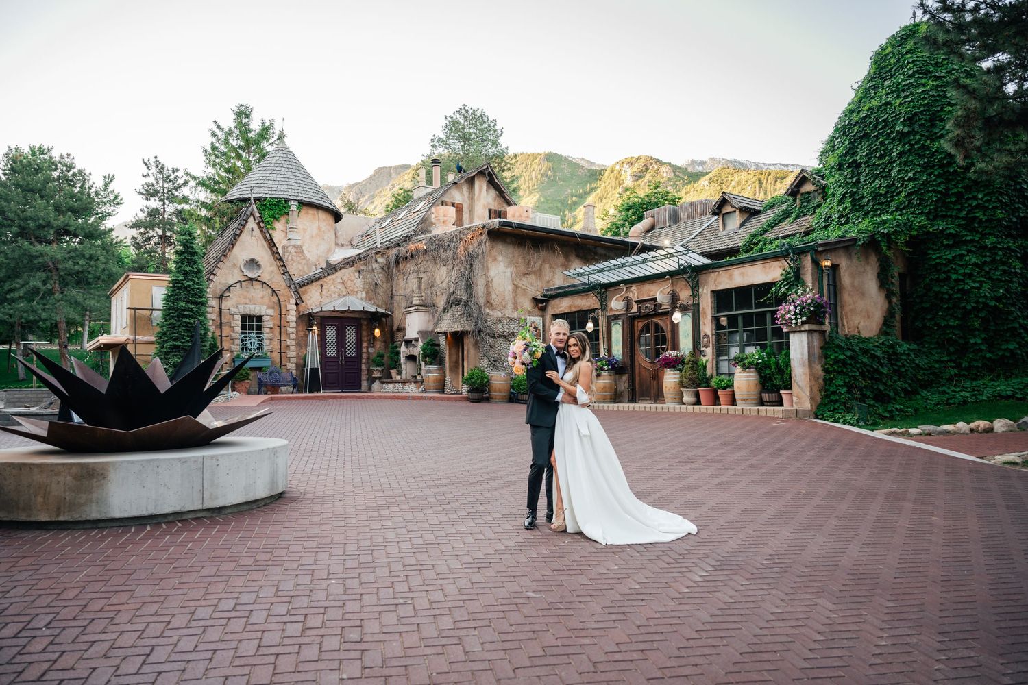 Wedding venue courtyard with brick paver patio surrounded by elegant stone buildings and lush landscaping.