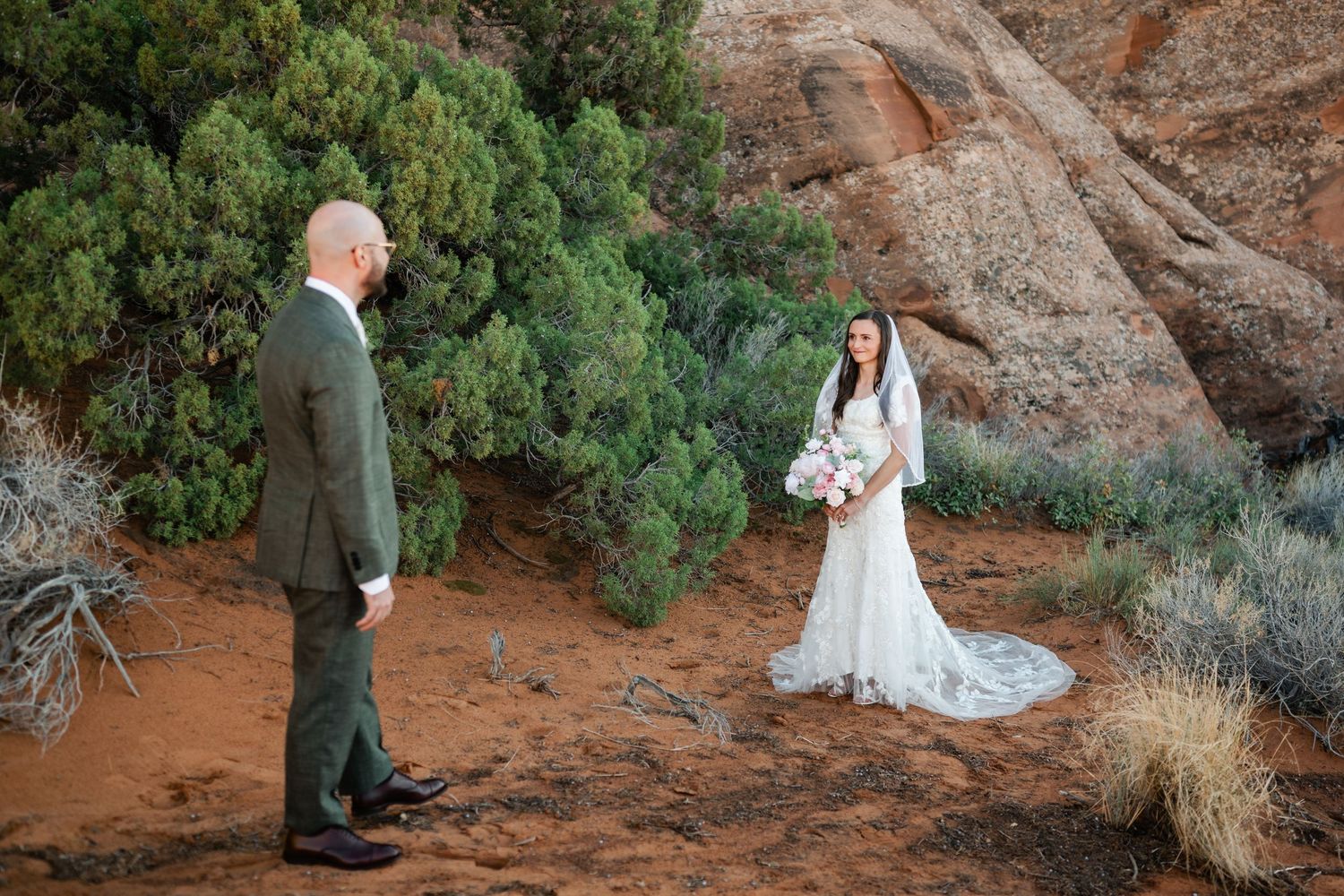 A wedding ceremony takes place against stunning red rock formations in a desert landscape.