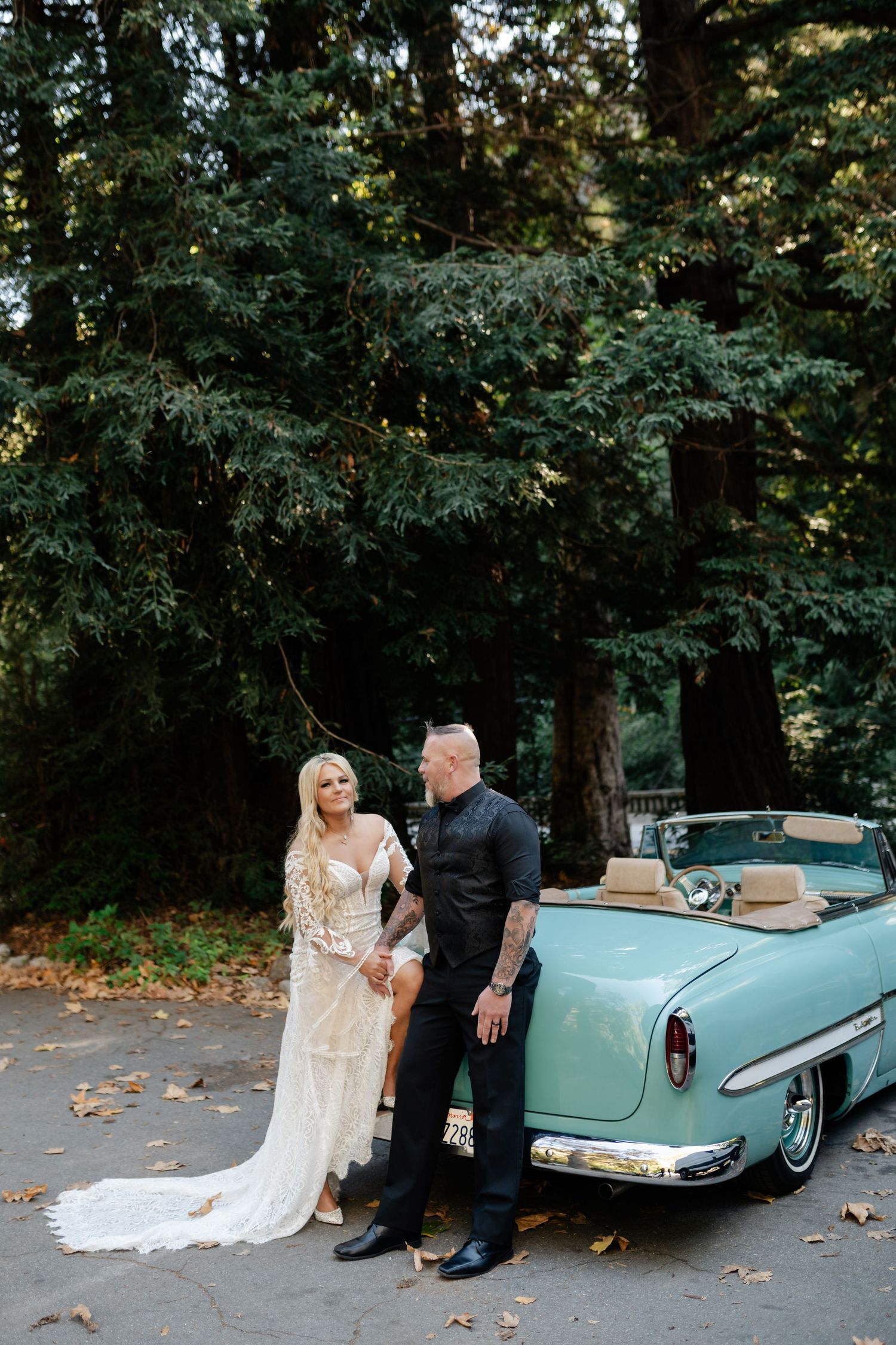 Classic turquoise convertible car serves as elegant backdrop for wedding photos.