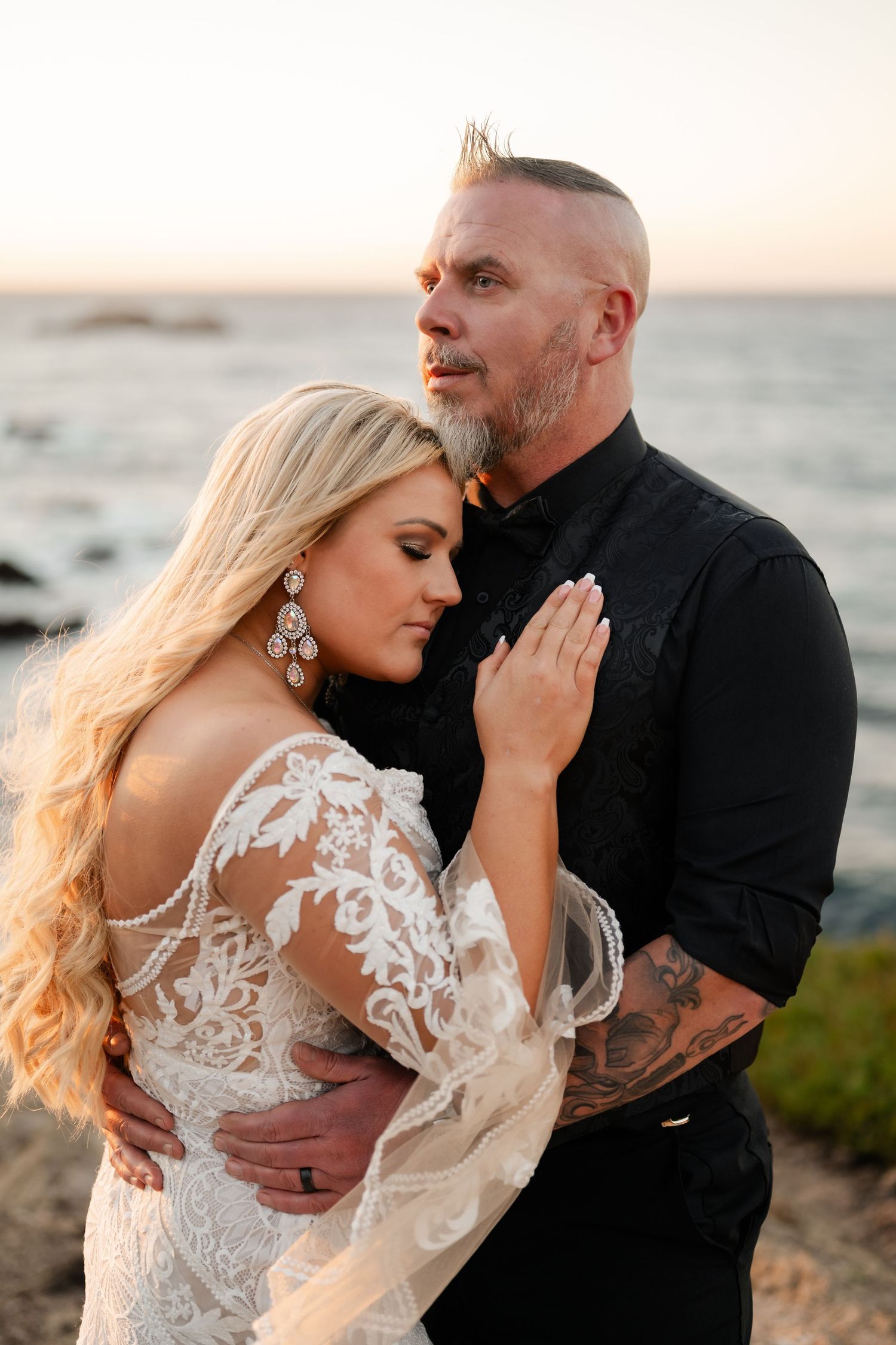 Couple embraces on coastal cliff during golden hour wedding photoshoot.