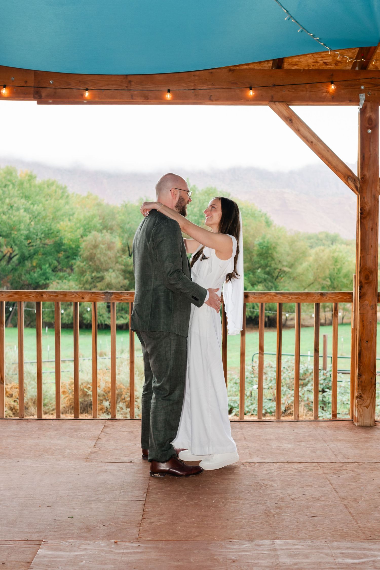 A couple dances together on a wooden pavilion deck overlooking a scenic mountain landscape.