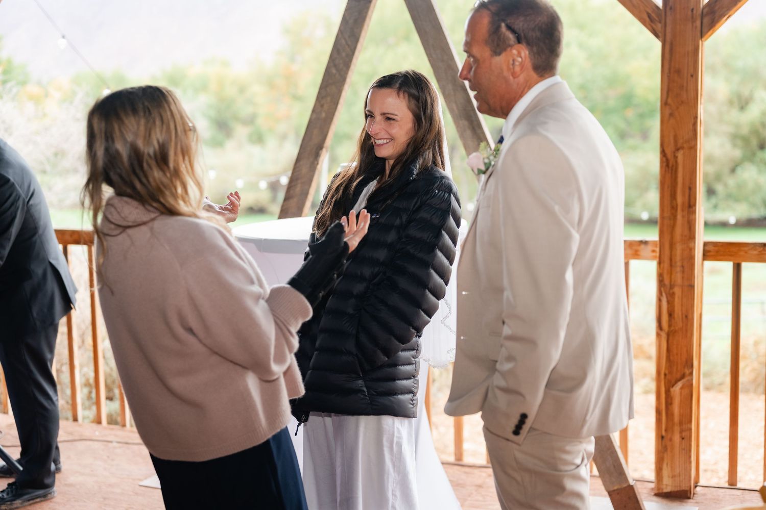 Wedding guests socialize during daytime reception on wooden deck with mountain views.