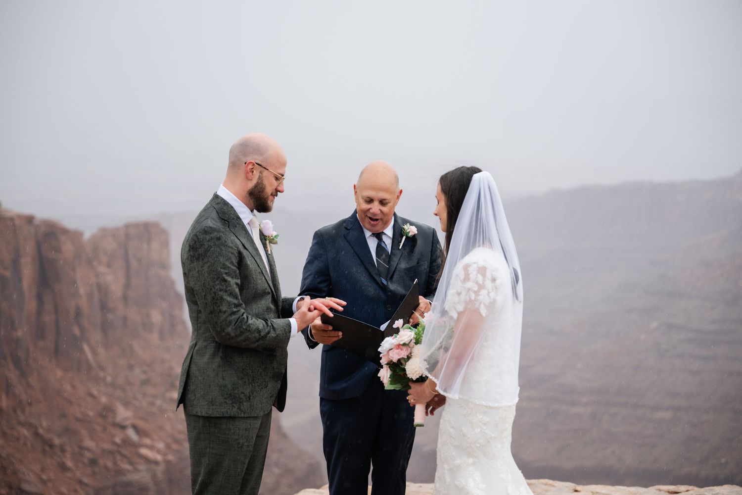 Intimate wedding ceremony taking place on edge of vast desert canyon landscape.