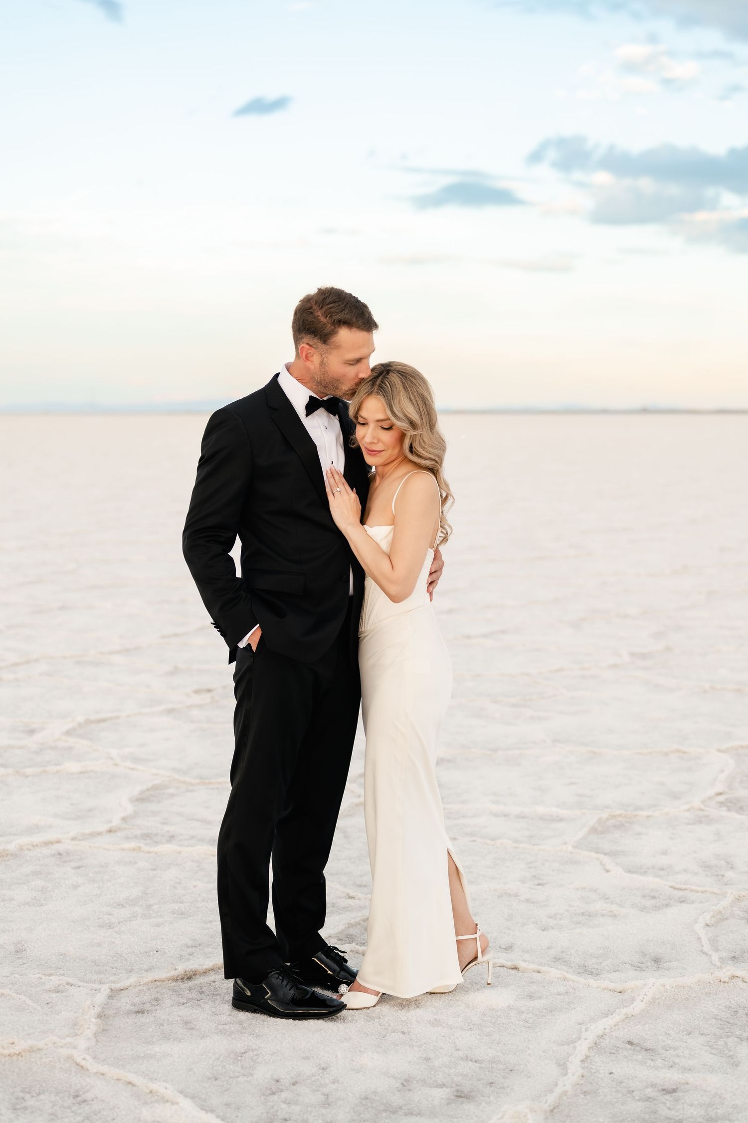 Salt Flats Elopement Photos. A romantic couple in formal attire embraces on a salt flat during sunset, creating an ethereal wedding photo.