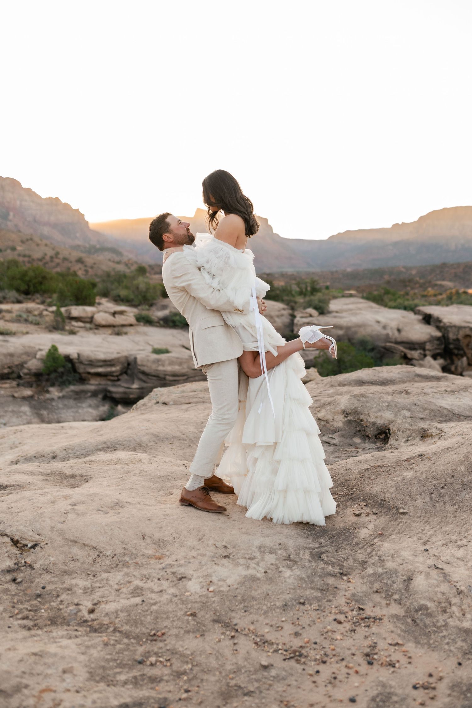 Romantic desert wedding photos on rocky terrain with mountain backdrop.