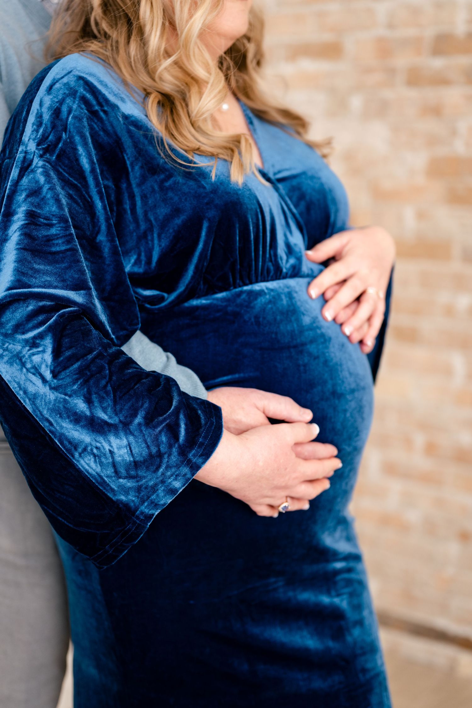Close-up views of a pregnant belly in a navy blue velvet dress against a brick wall background.
