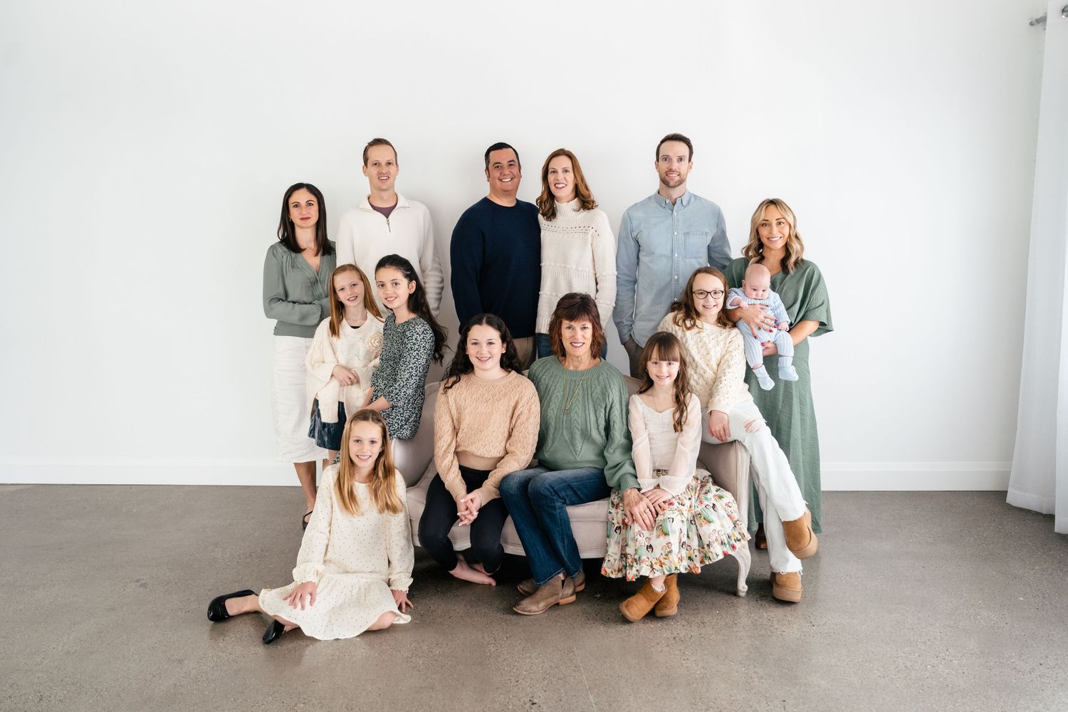A group in coordinated neutral-toned outfits poses together against a white wall in a studio setting.