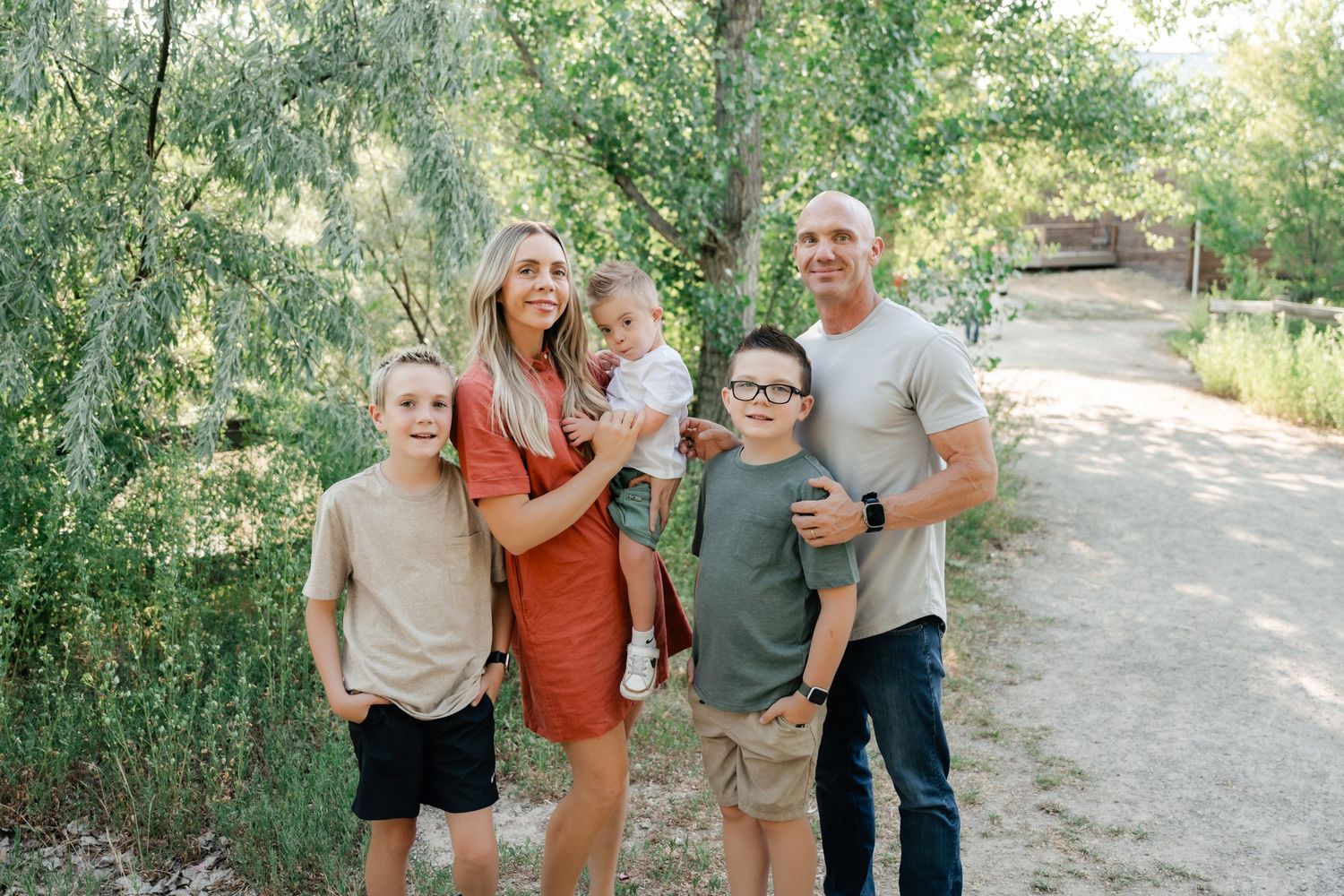 A group of people laugh and embrace while walking together on a dirt path surrounded by green foliage.
