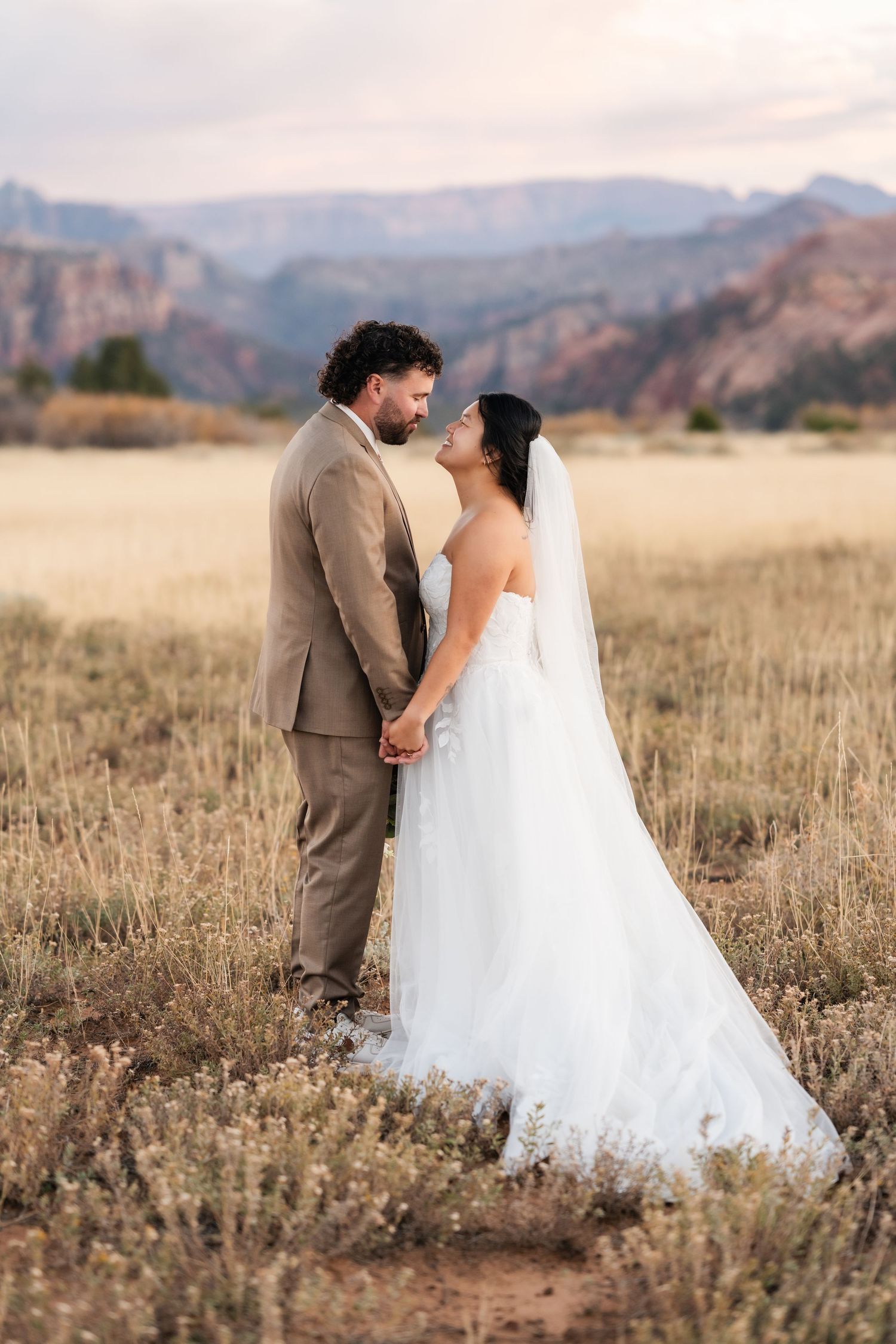 Newlyweds share an intimate moment in a rustic field with mountain views.