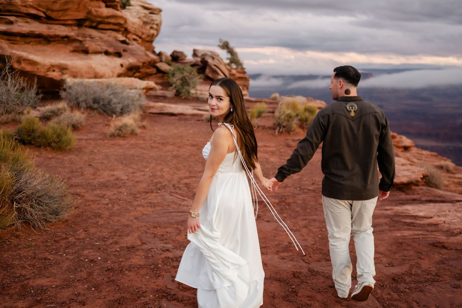 A couple holds hands while exploring the red rock formations at sunset in a desert landscape.